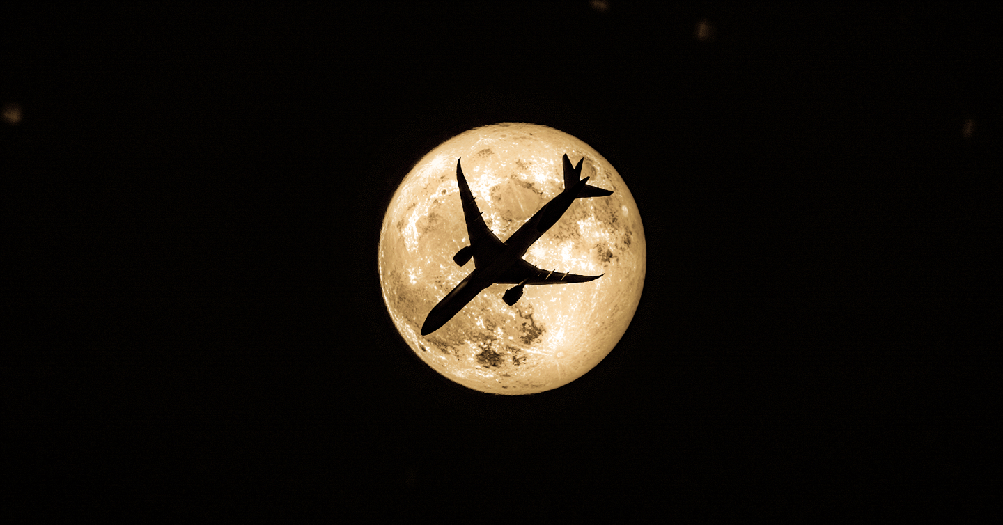 Plane silhouette in front of a giant yellow moon 