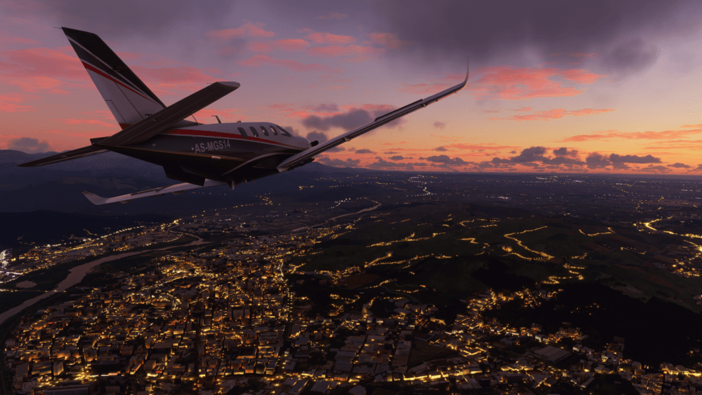A plane flies over a lit city at sunset.
