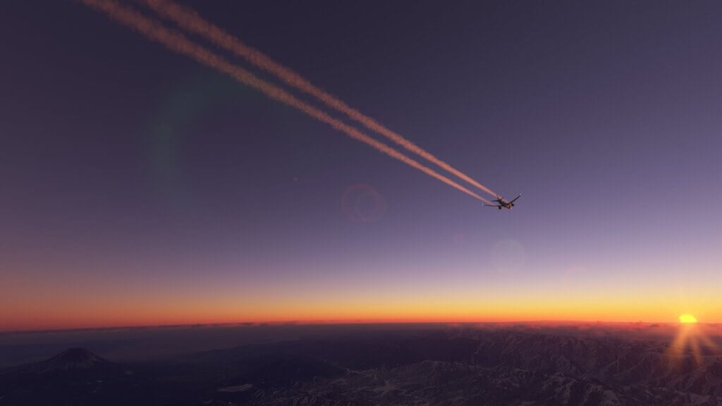 A condensation trail follows behind a plane that flies towards the sunset.