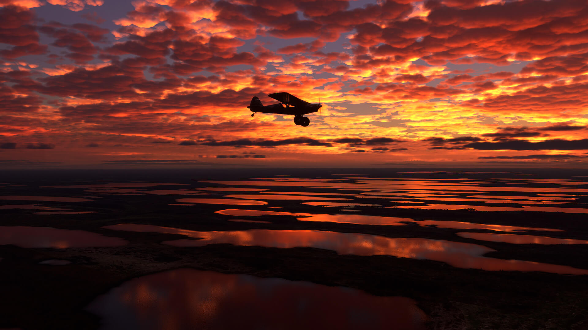 A fiery red and yellow sunset reflects on several lakes, and casts a lone plane in silhouette.