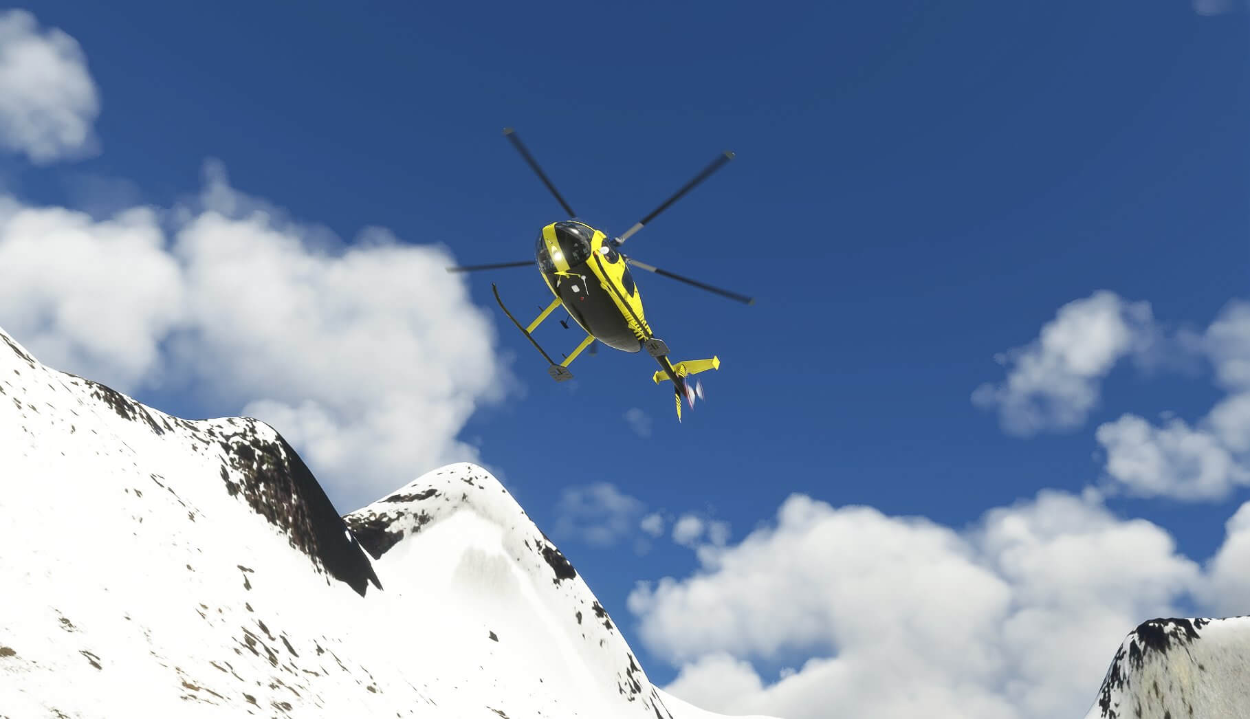 A bottom-up view of a yellow and black helicopter flying over snowy mountain scenery.