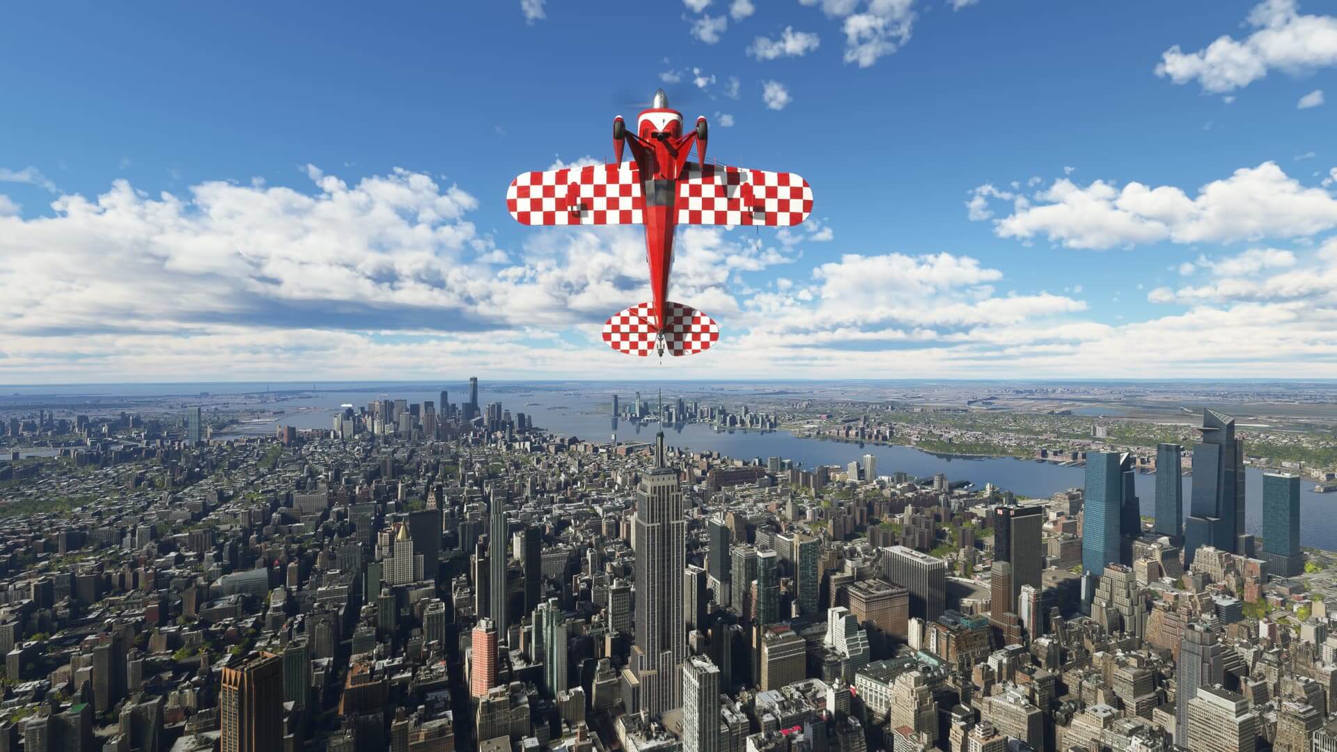 A Pitts Special flies straight up over Manhattan. The Empire State Building is visible under the plane. The camera is positioned such that the bottom wing and landing gear of the Pitts is visible.