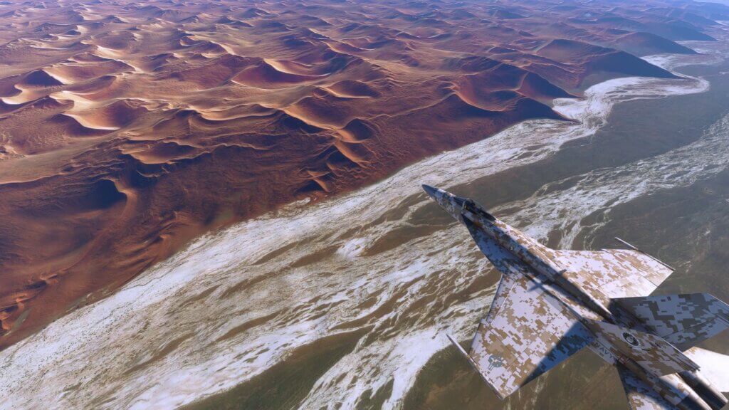 A Boeing F/A-18 Super Hornet with a desert camouflage paint scheme flies over a desert.
