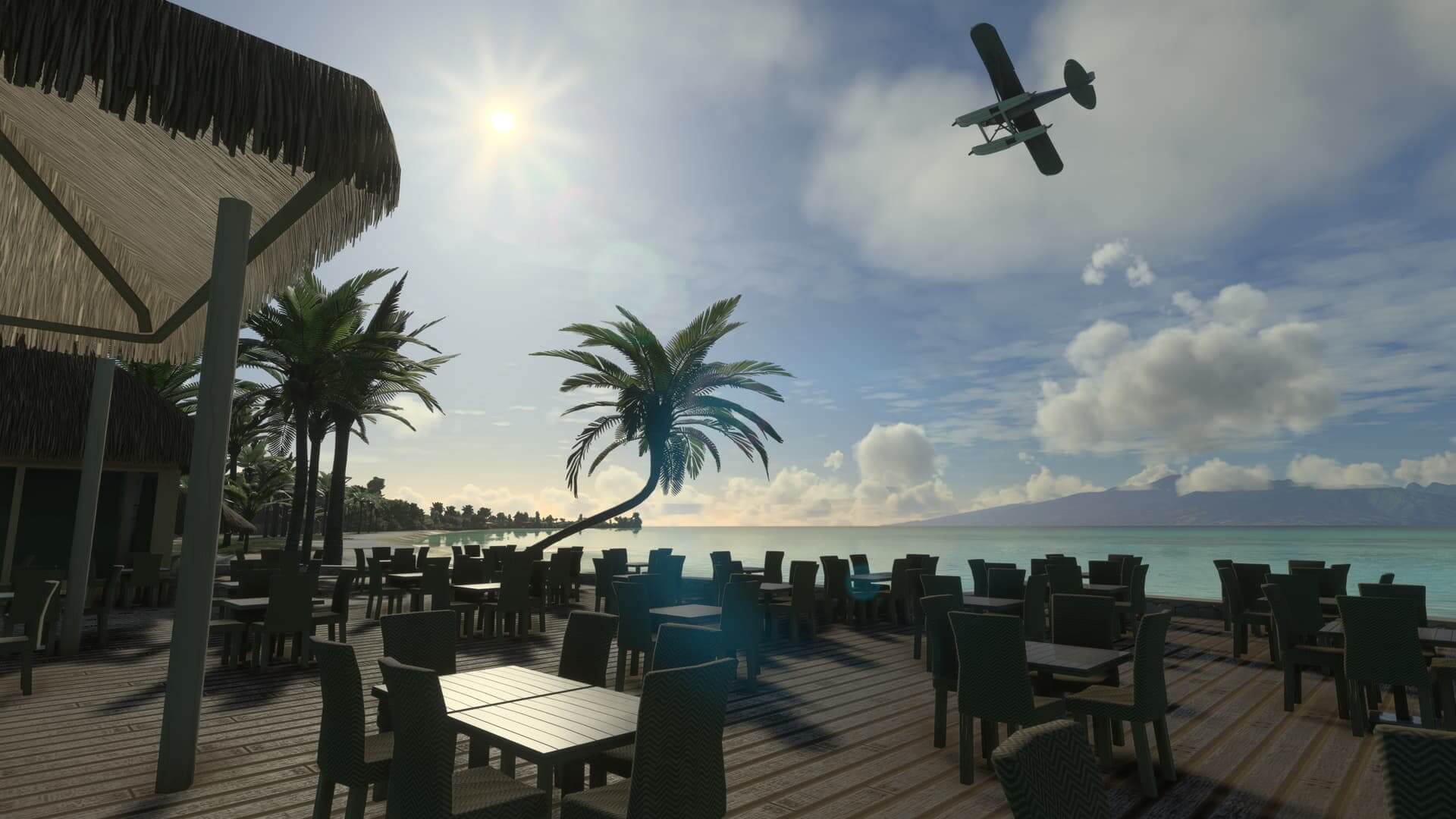 A plane with floats is in a steep banking turn as it flies above an outdoor resort restaurant. There are palm trees, a beach, and green/blue water in the background.