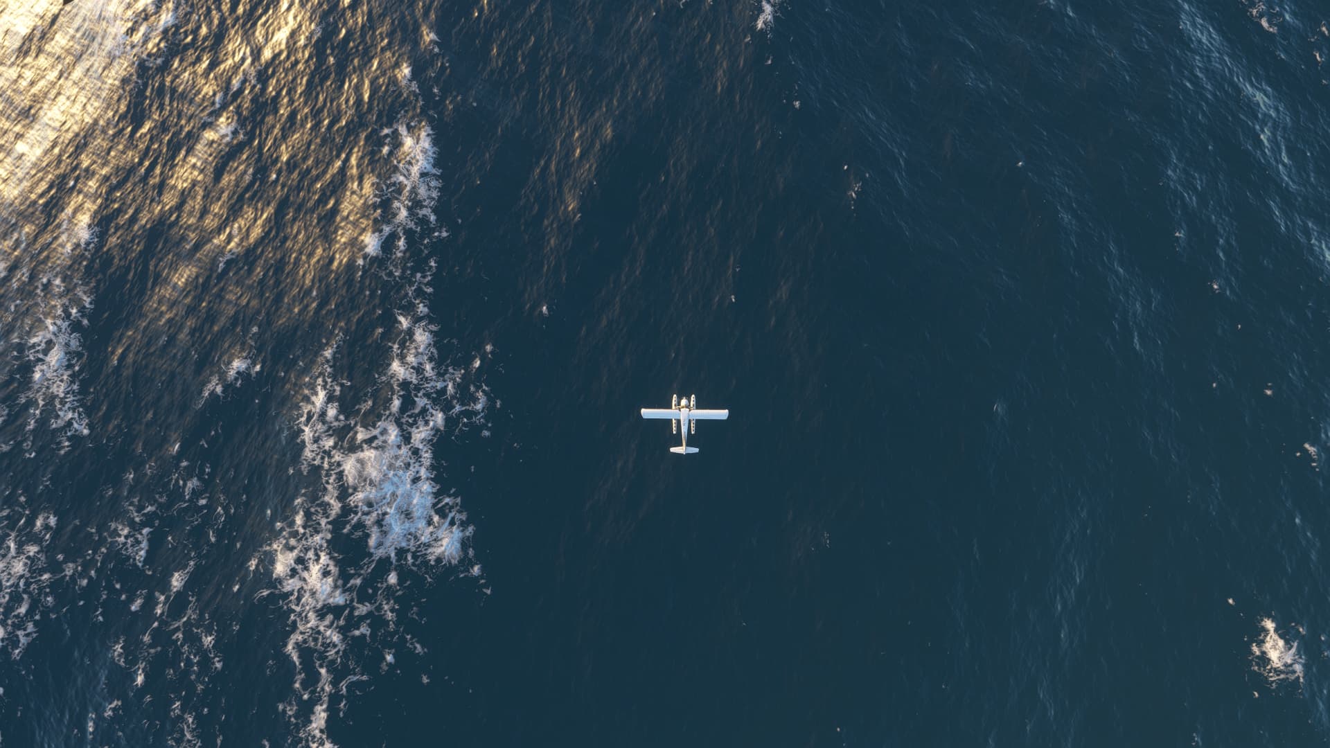 Top down view of a single-engine GA plane equipped with floats flying over the open sea.