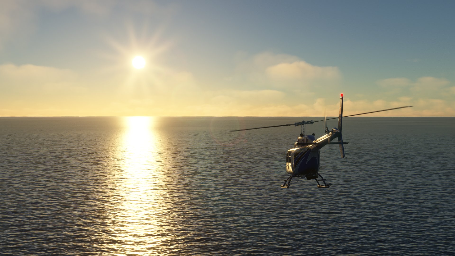 A Bell 407 helicopter flies towards the sunset over the open seas.