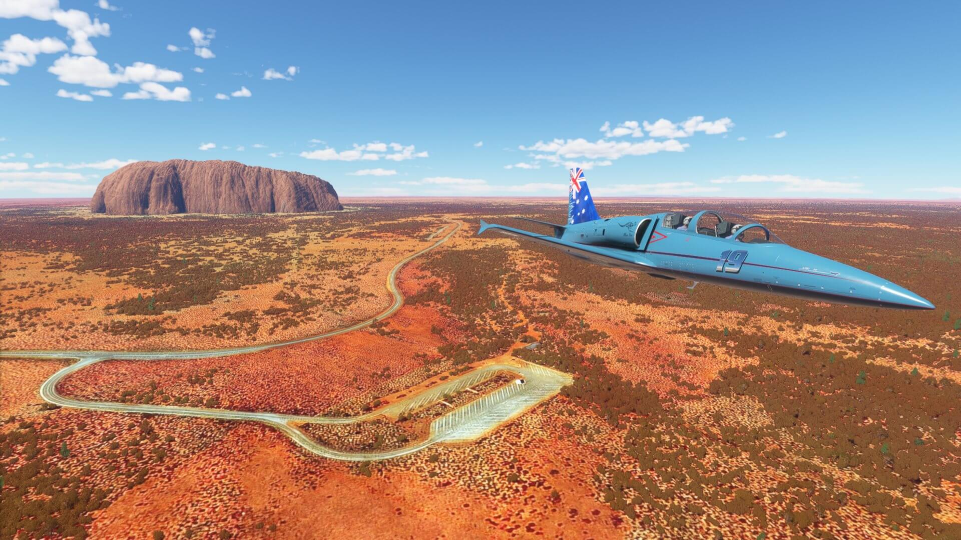 An Australia-themed L29 passes overhead a deserted car park linked to a road heading towards Ayers Rock