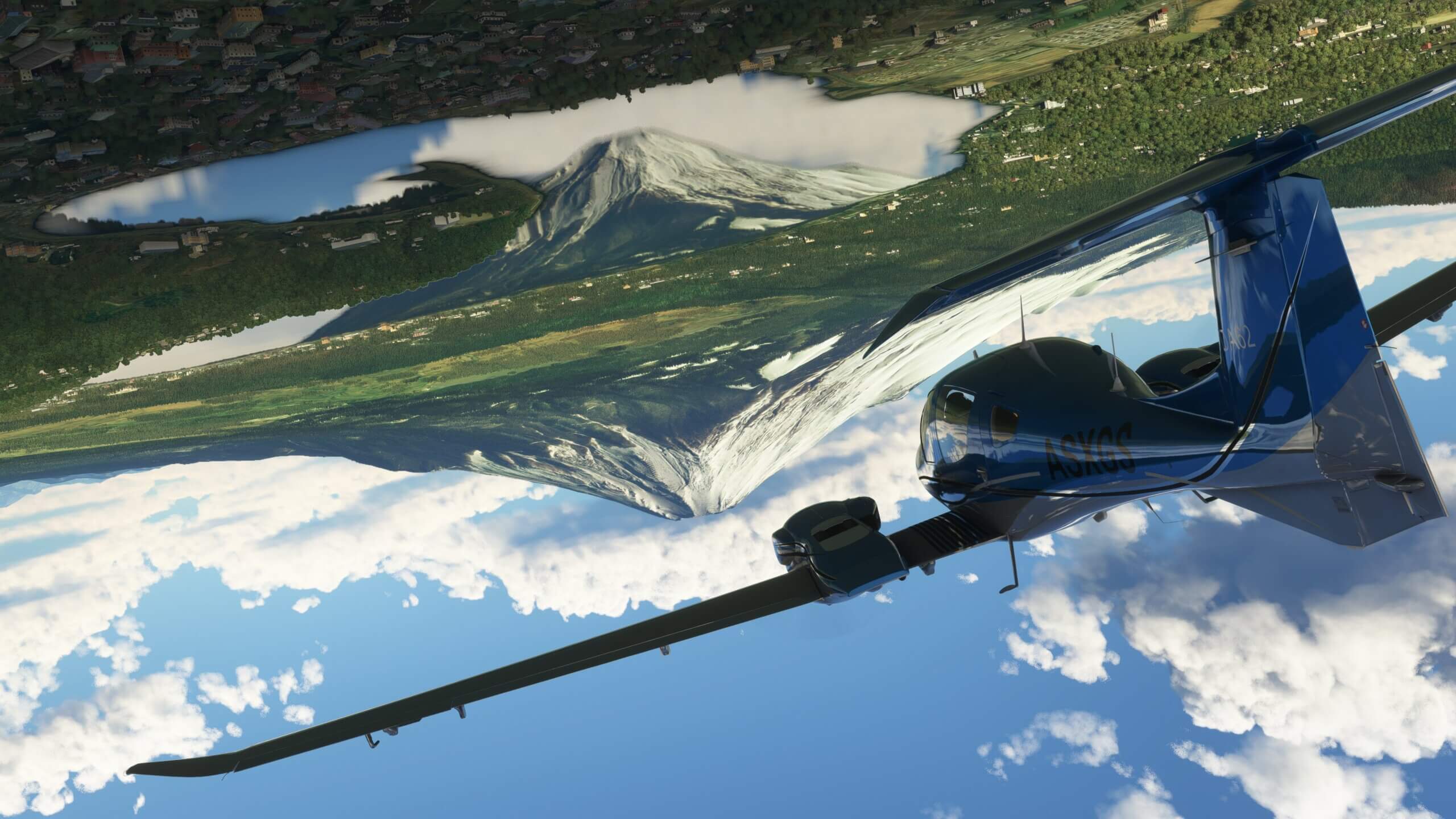 A DA-62 heads towards a Volcano whilst flying inverted, as the image of the Volcano is reflected on a lake below.