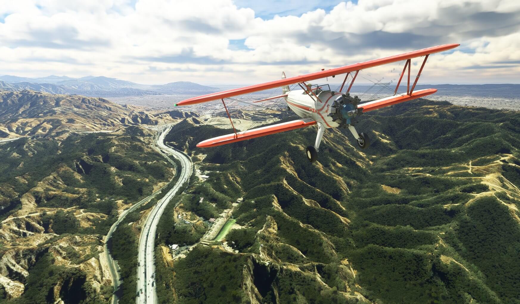 An orange and white bi-plane stays clear of high terrain below with a bustling intersection weaving its way through the valley