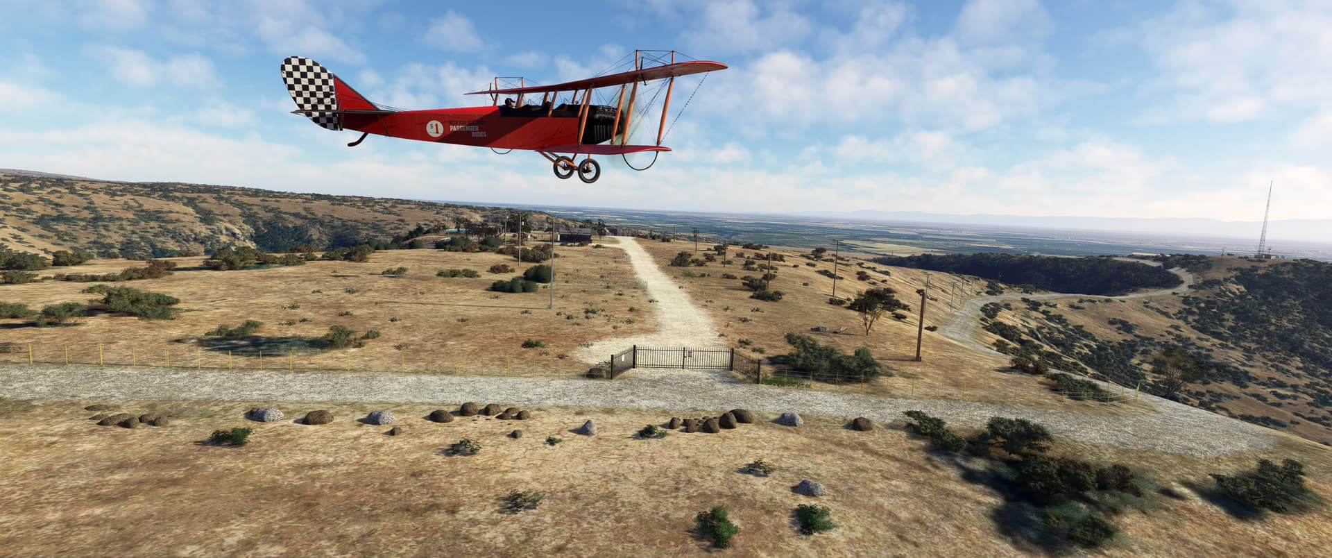 A vintage red colored bi-plane flies low and level over a desert ranch