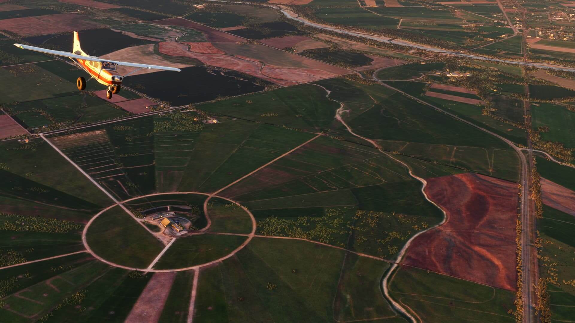 A high-wing Cessna banks to the left as it flies over farmland, with weaving dirt tracks cutting through the fields