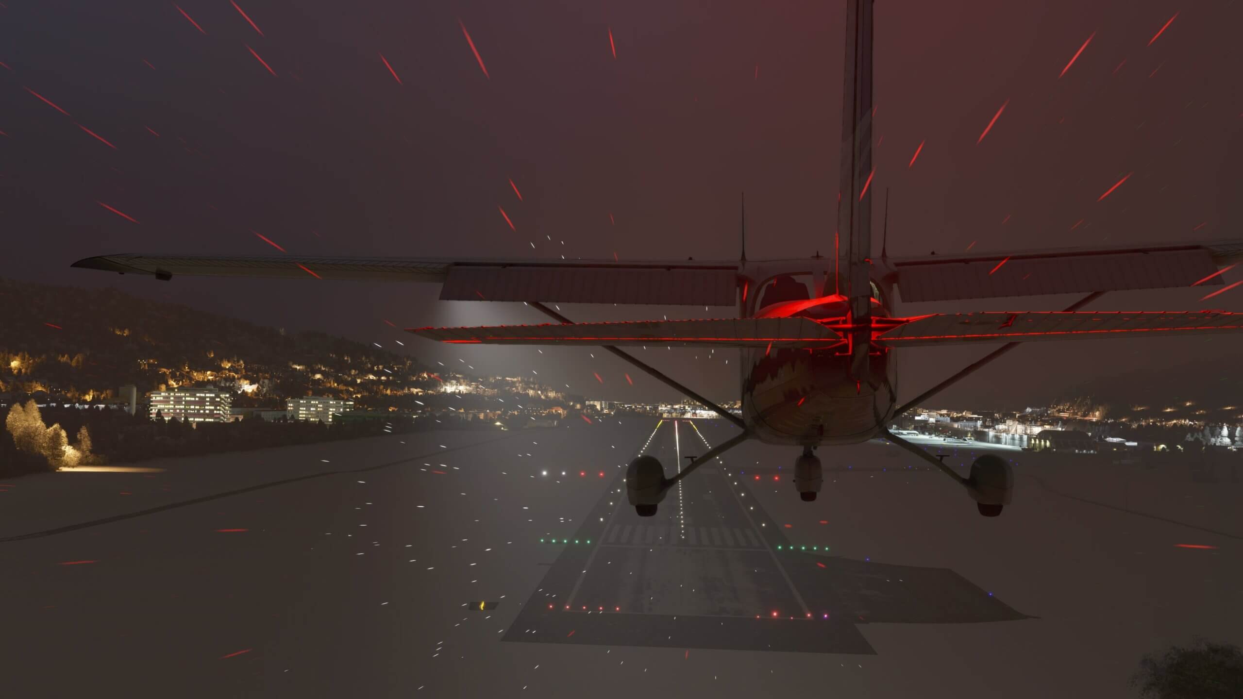 A Cessna comes into land at night with snow covering the airport apron.
