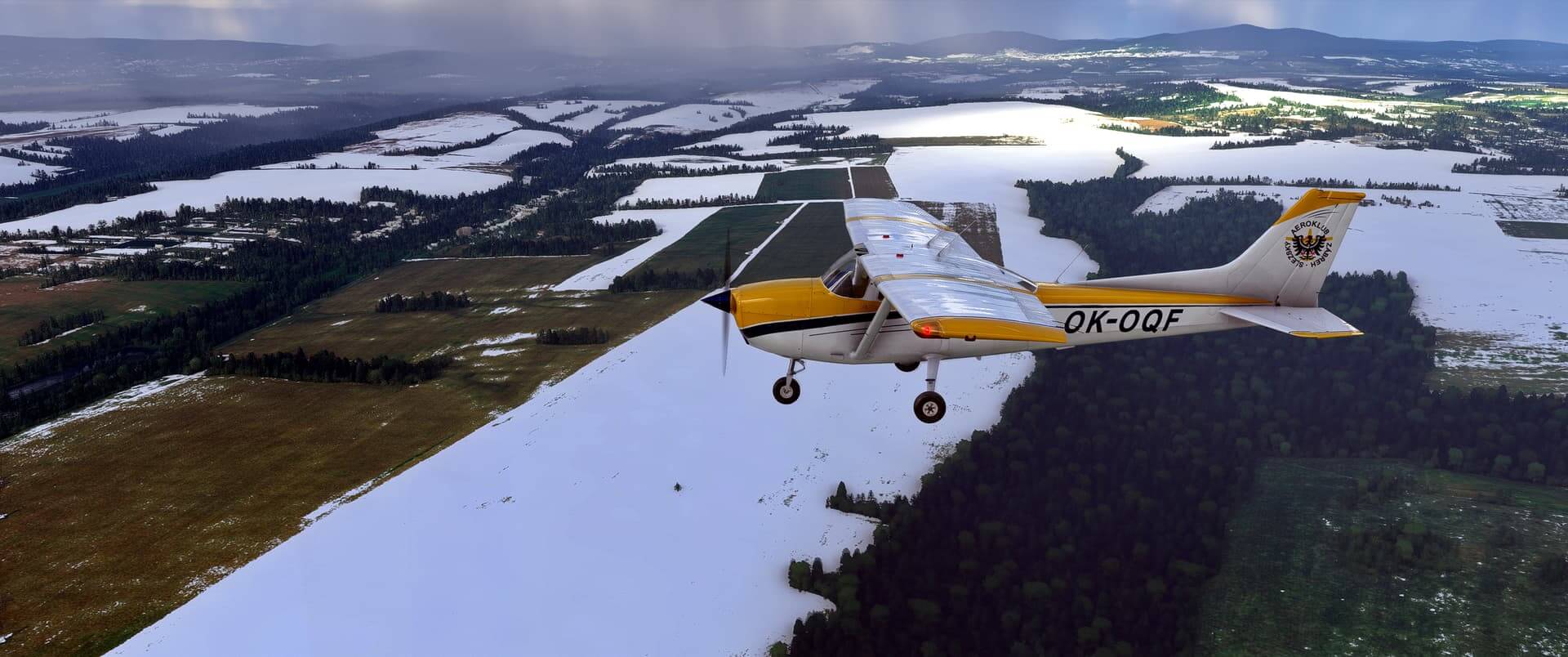 A Cessna flies over flat fields with some covered with snow.