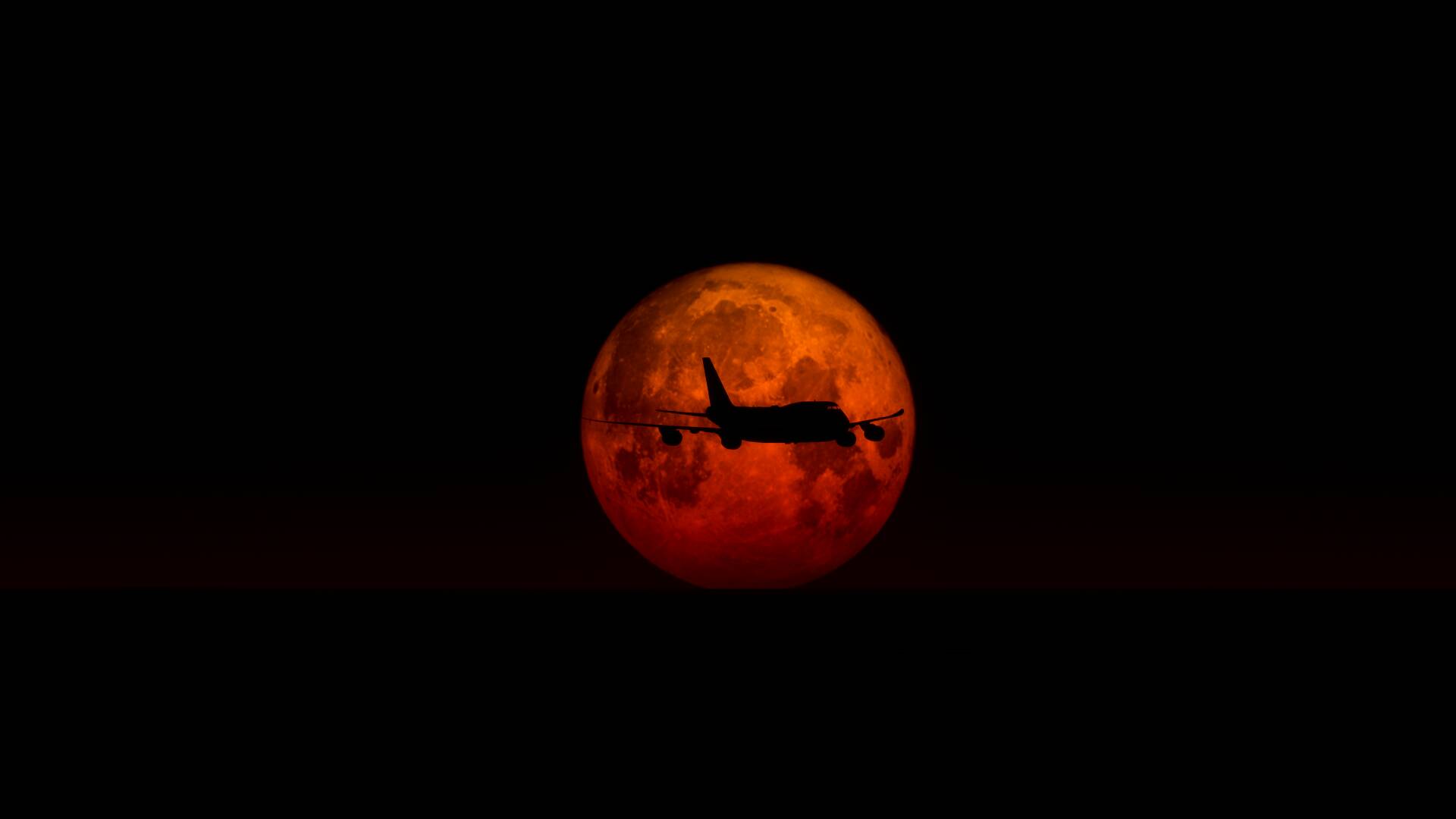 A Boeing 747 silhouetted by a blood orange moon.