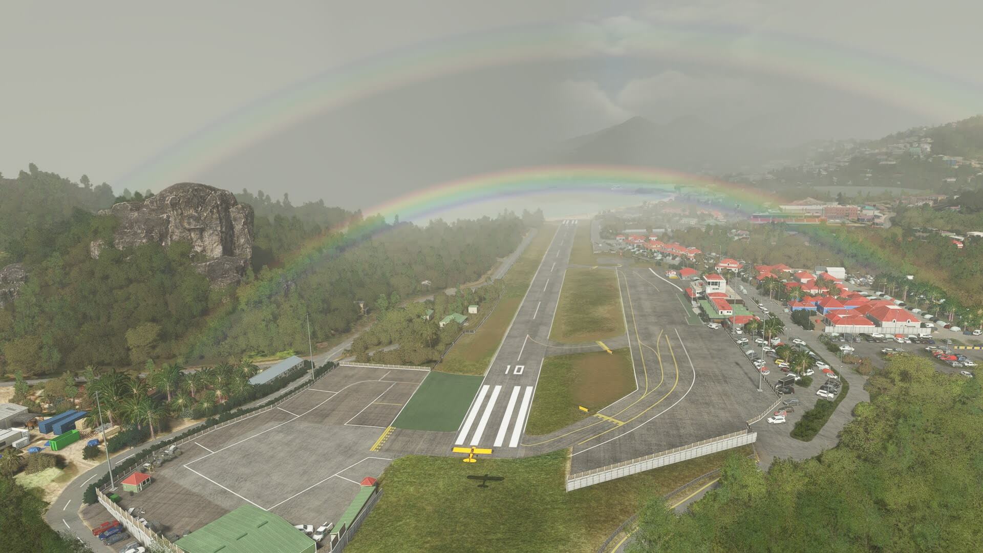 An Extra Cub flies over the threshold at St. Baarts, with a double rainbow above the airport.