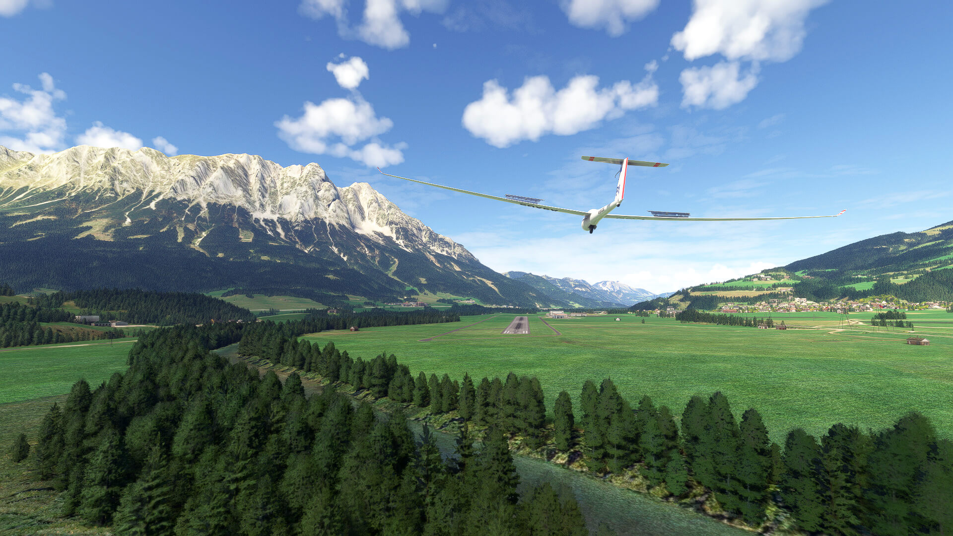 A glider with spoilers deployed and landing gear down approaches a runway in a valley.