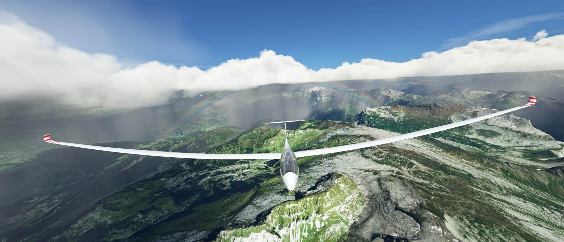 A glider soars above mountains with clouds and a rainbow behind.
