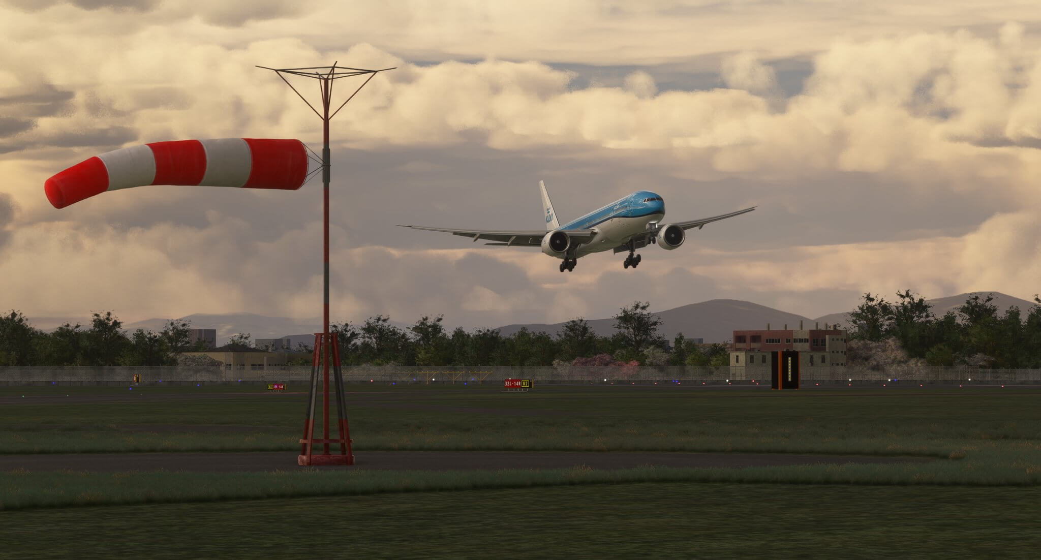 A KLM Boeing 777 with landing gear and flaps lowered on short final to land, with a wind sock next to the runway showing strong gusts.