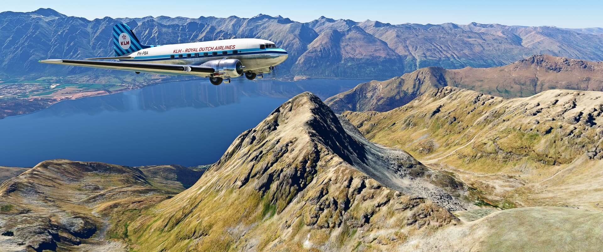 A KLM Royal Dutch Airlines DC-3 flies level over the top of undulating terrain, with a large lake visible behind the aircraft
