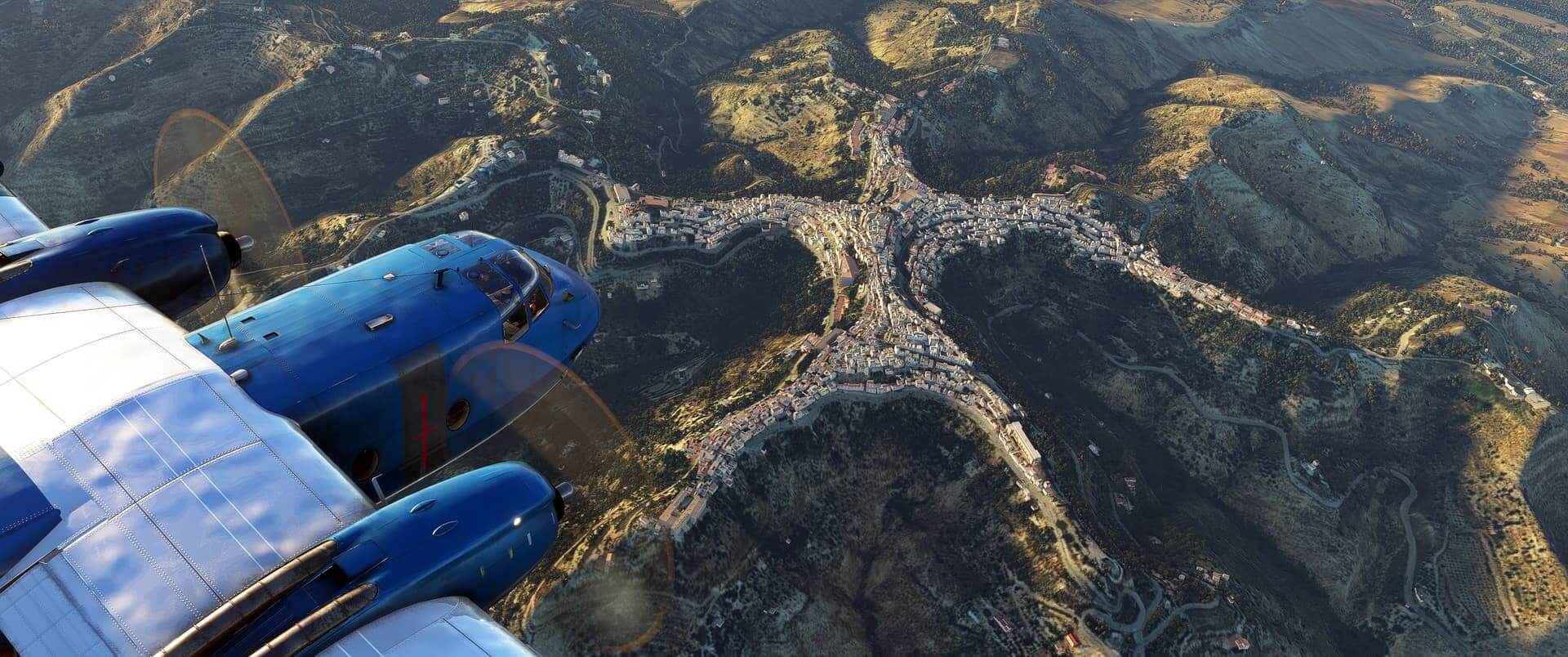 A blue dual-prop high-wing aircraft flies above a city located on top of mountain ridges