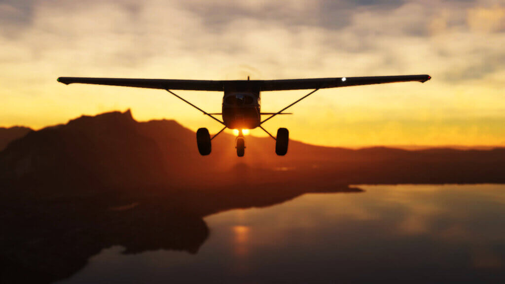 A Cessna 172 cruises in straight and level flight, with mountains behind and the sun peaking out from the crest of a hill.