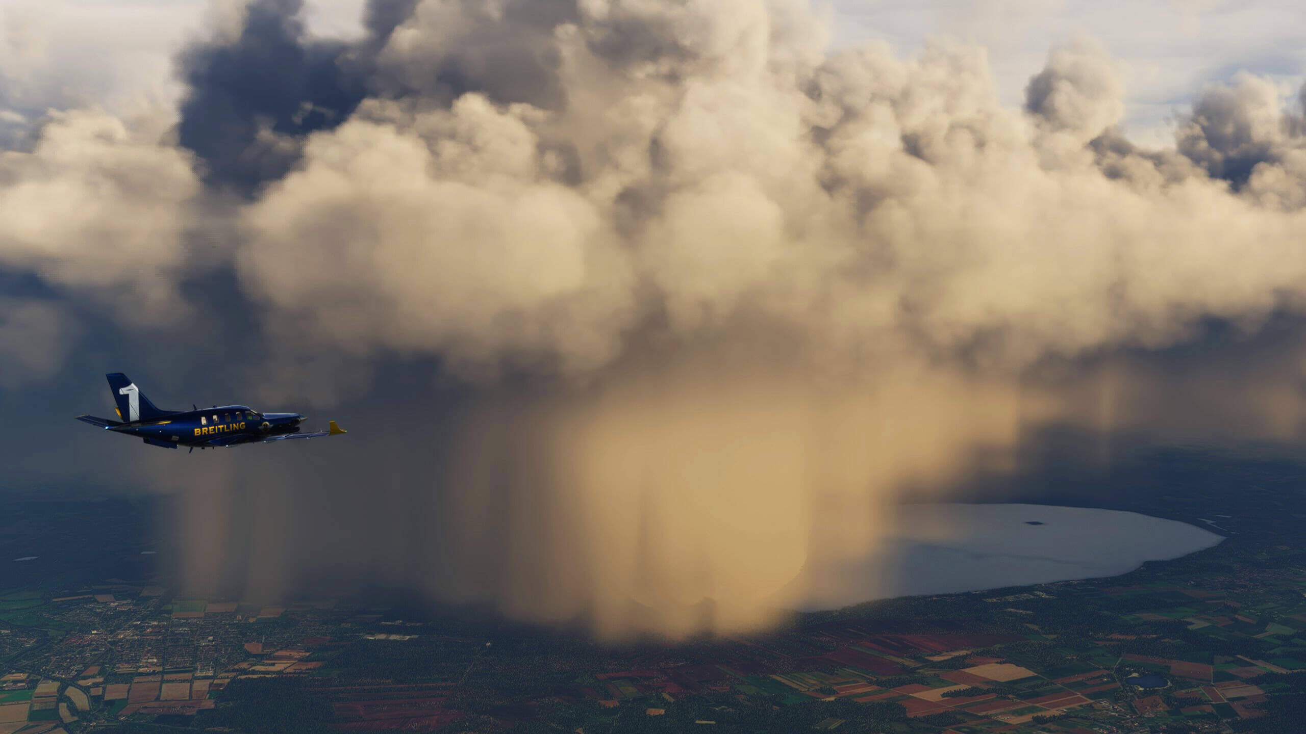 A turboprop in blue and yellow Breitling paint flies straight and level approaching thick cloud ahead, with heavy rain falling to the fields below.