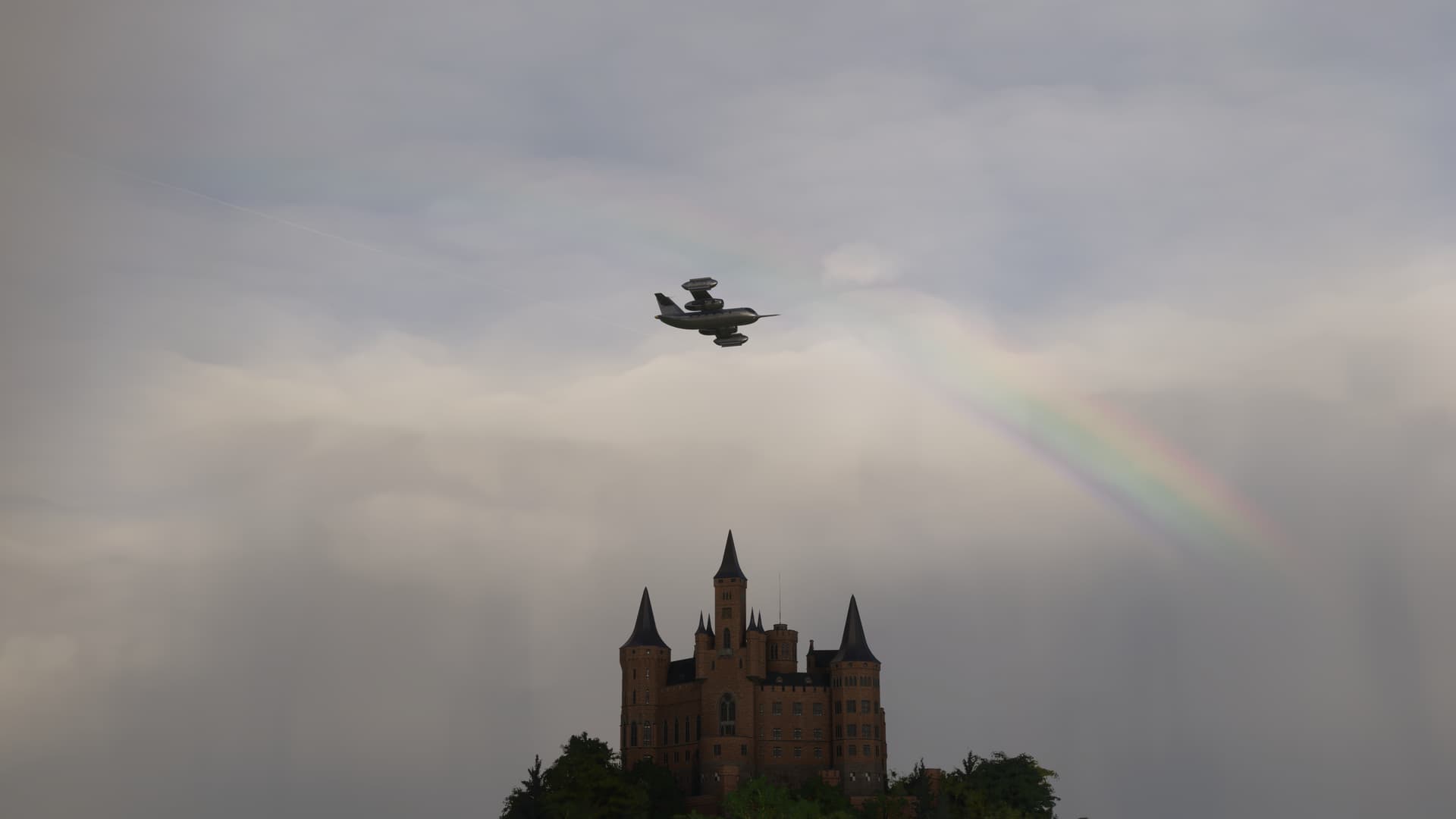 The Dornier Do-31 flies overhead a castle with a rainbow peaking through the clouds behind