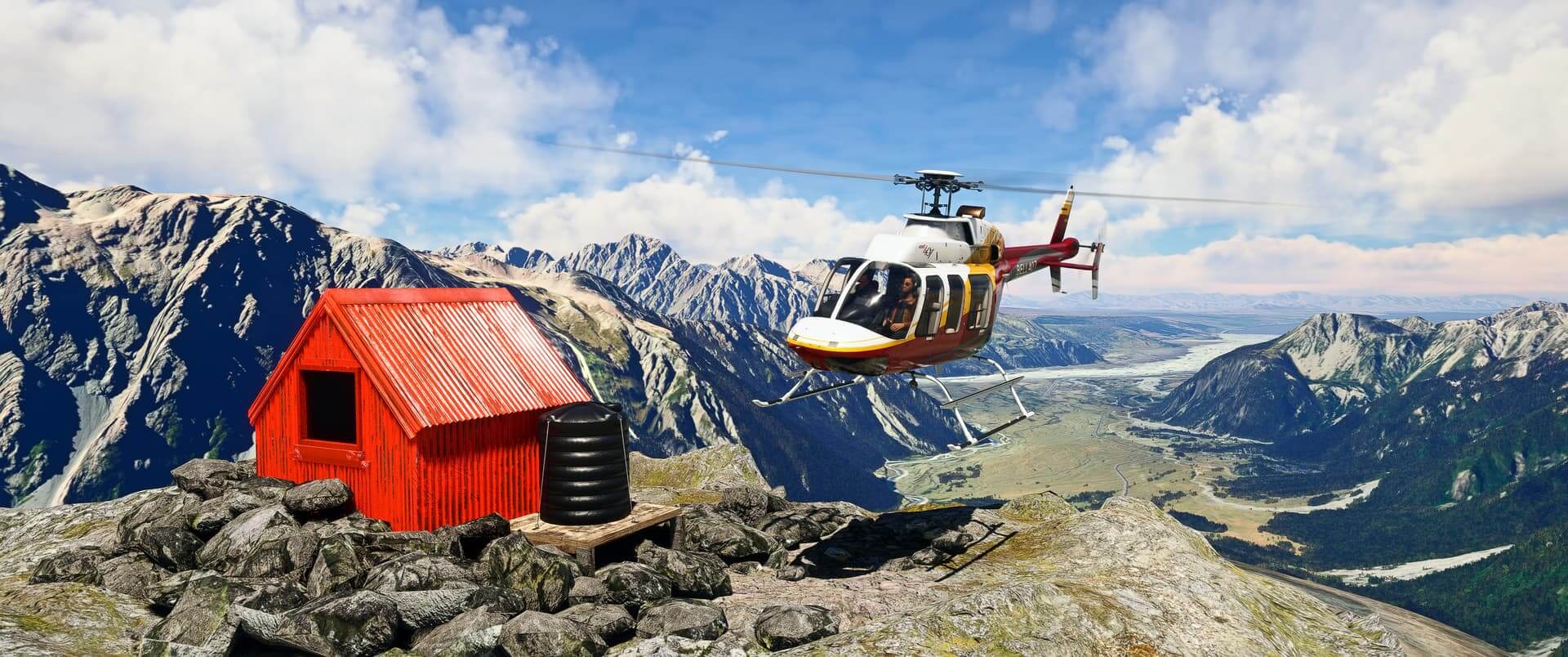 A Bell 407 hovers close to a red tin hut located on a mountain top, with a huge valley located behind