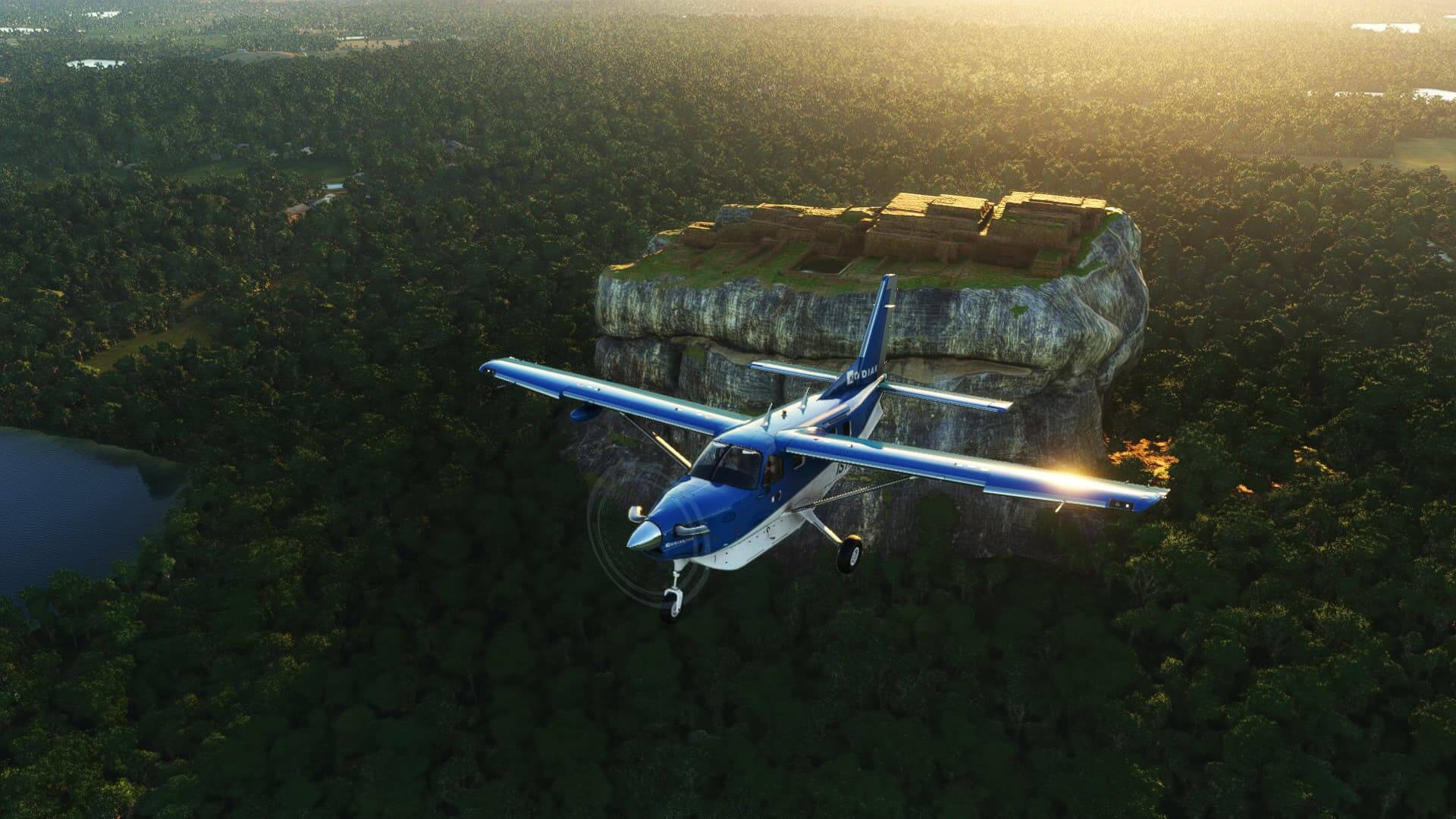 A high-wing propeller aircraft in blue and white paint over a monument located on a high rocky plateau, with dense forest trees below