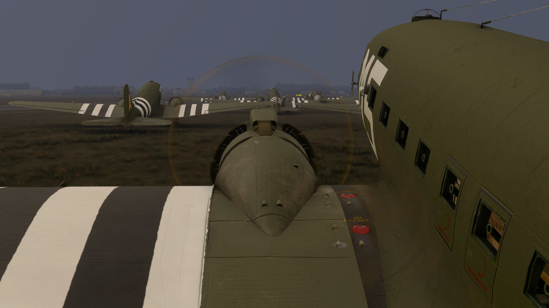 A line of C-47D Skytrain aircraft all following one another whilst taxiing on a grass runway strip.