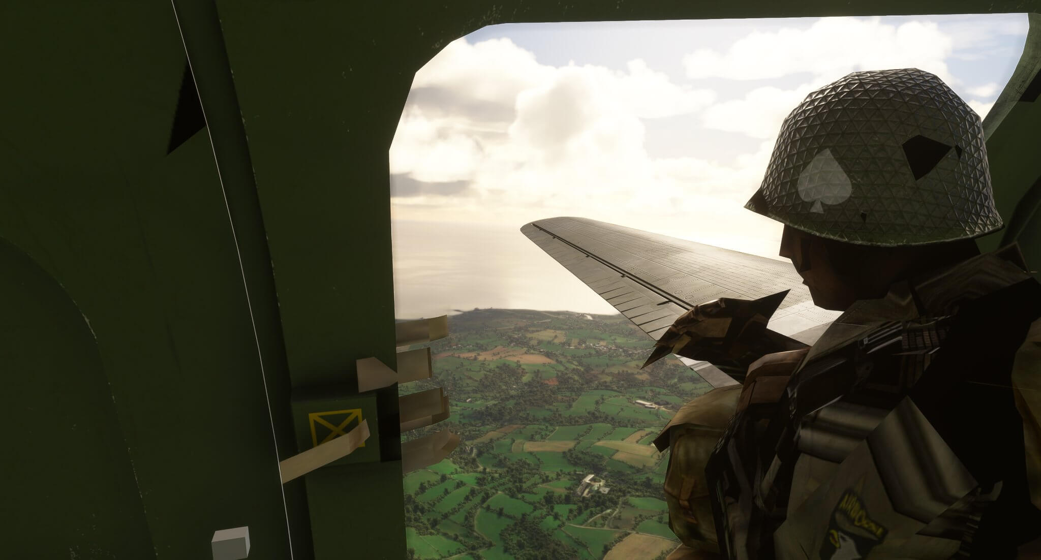 A Paratrooper looks out of the open door of a C-47D Skytrain, which is in flight above green fields.