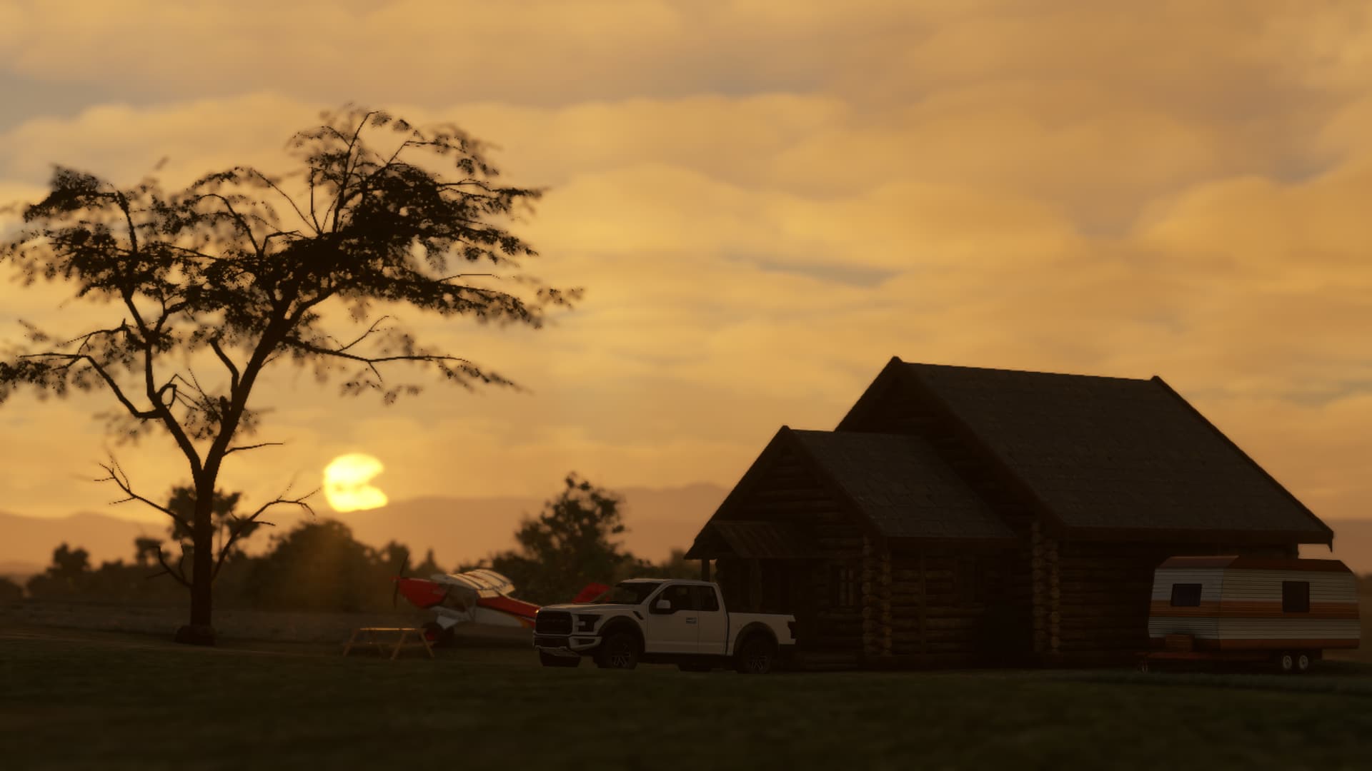 The sun sets in the background of a country lodge with vehicles parked outside