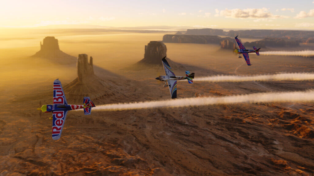 Three Extra aerobatic aircraft plume smoke from their tails as they bank left in close formation, whilst flying above a desert
