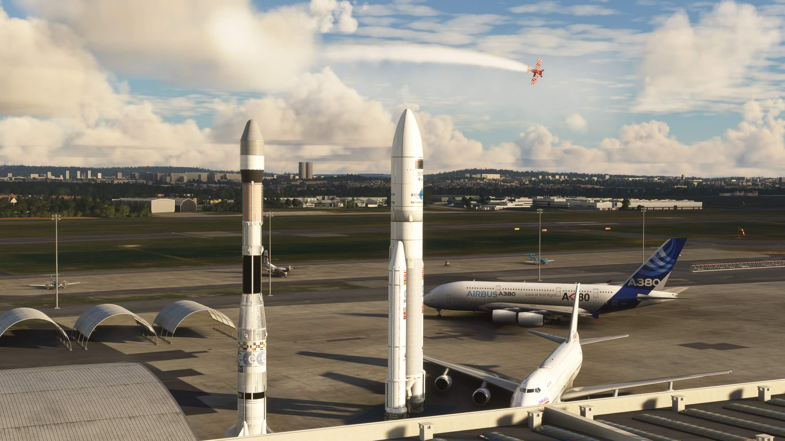 A red and white chequered propeller aircraft trials smoke whilst flying over a busy airport apron with airliners and space rockets on display