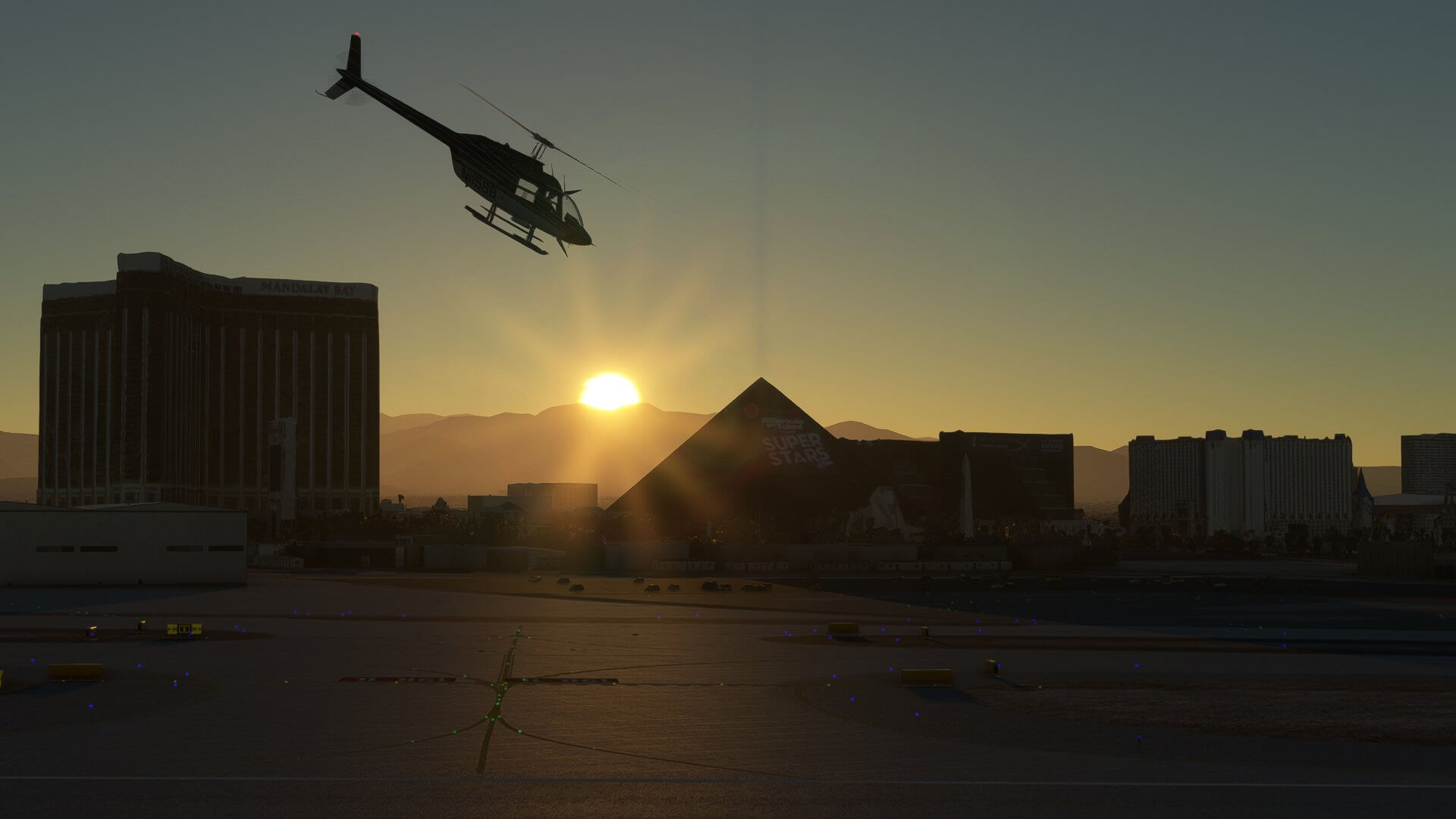 A Bell 407 Helicopter flies at Las Vegas airport with the silhouette of the Las Vegas strip visible behind as the sun rises behind the mountains in the distance