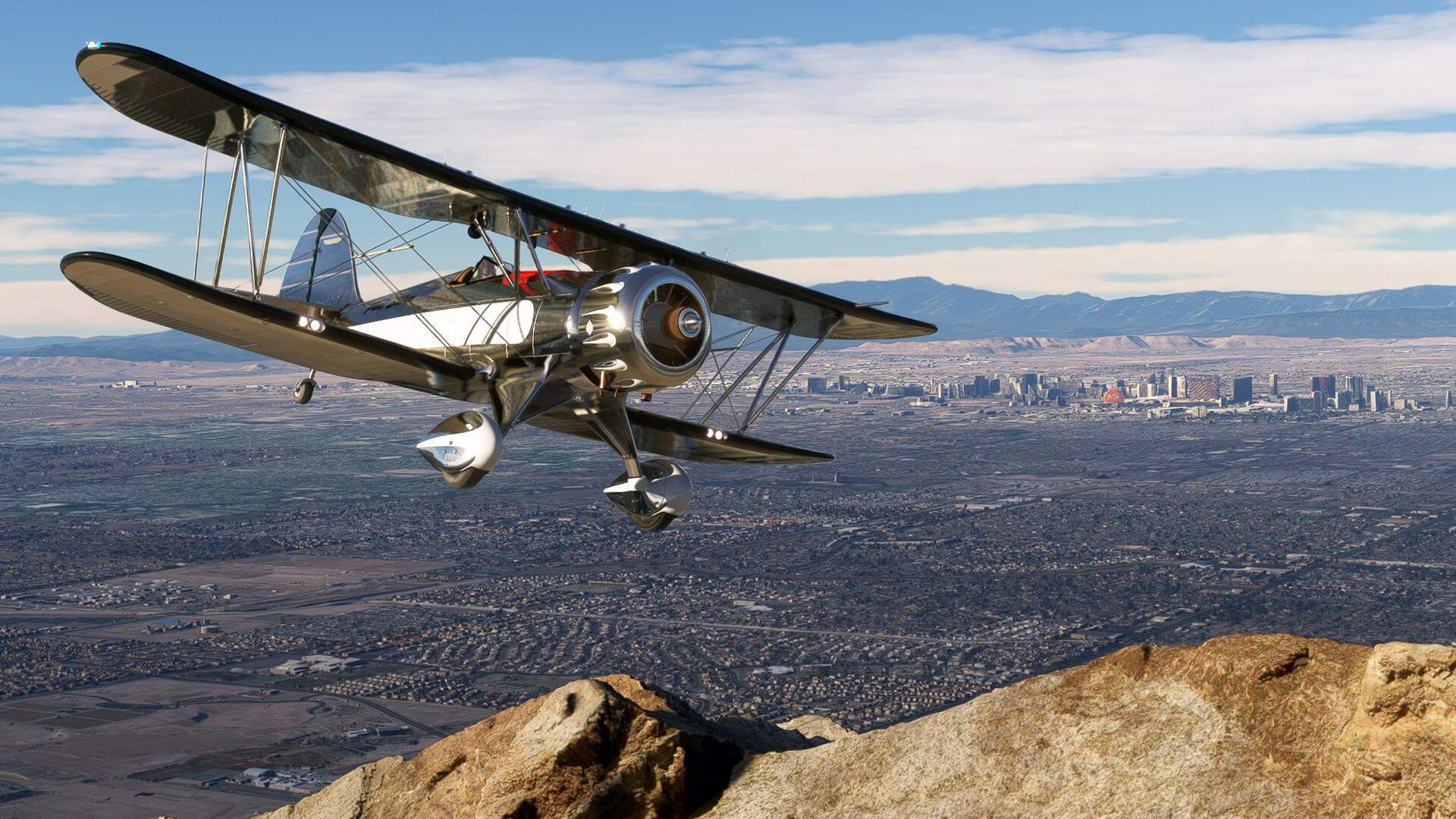 A dual wing silver propeller plane avoids terrain whilst banking left with the city of Las Vegas visible in the distance