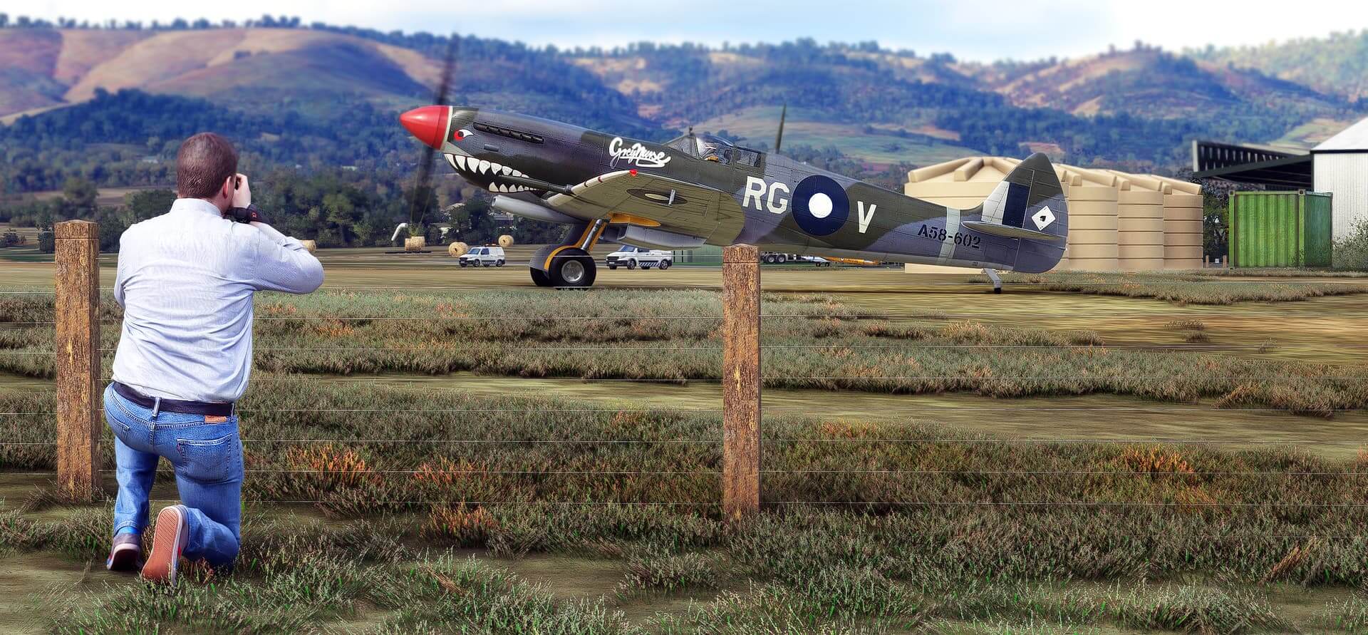 A photographer kneels to take a picture of a World War 2 fighter parked on a grass apron