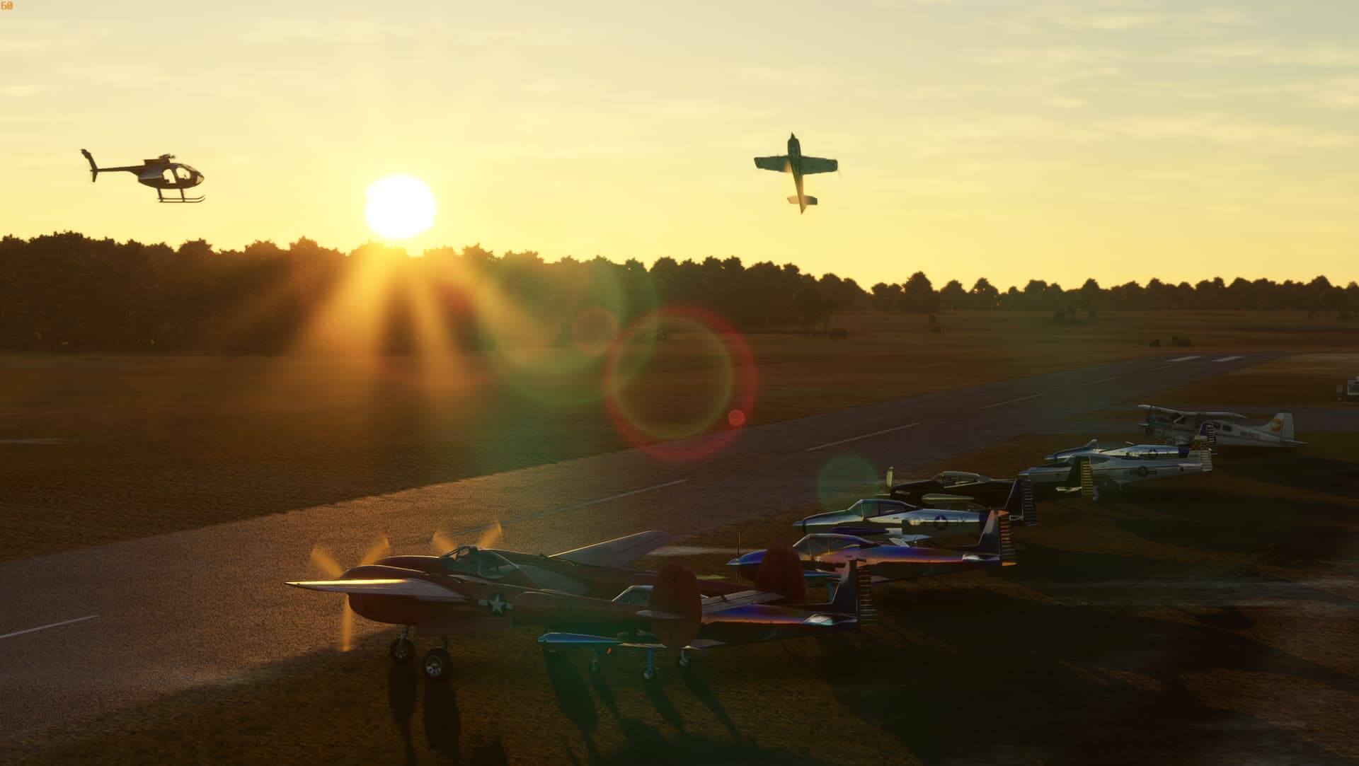 An Extra 330 pulls up into the vertical next to a helicopter, as the sun sets on an airshow with parked aircraft on the ramp below