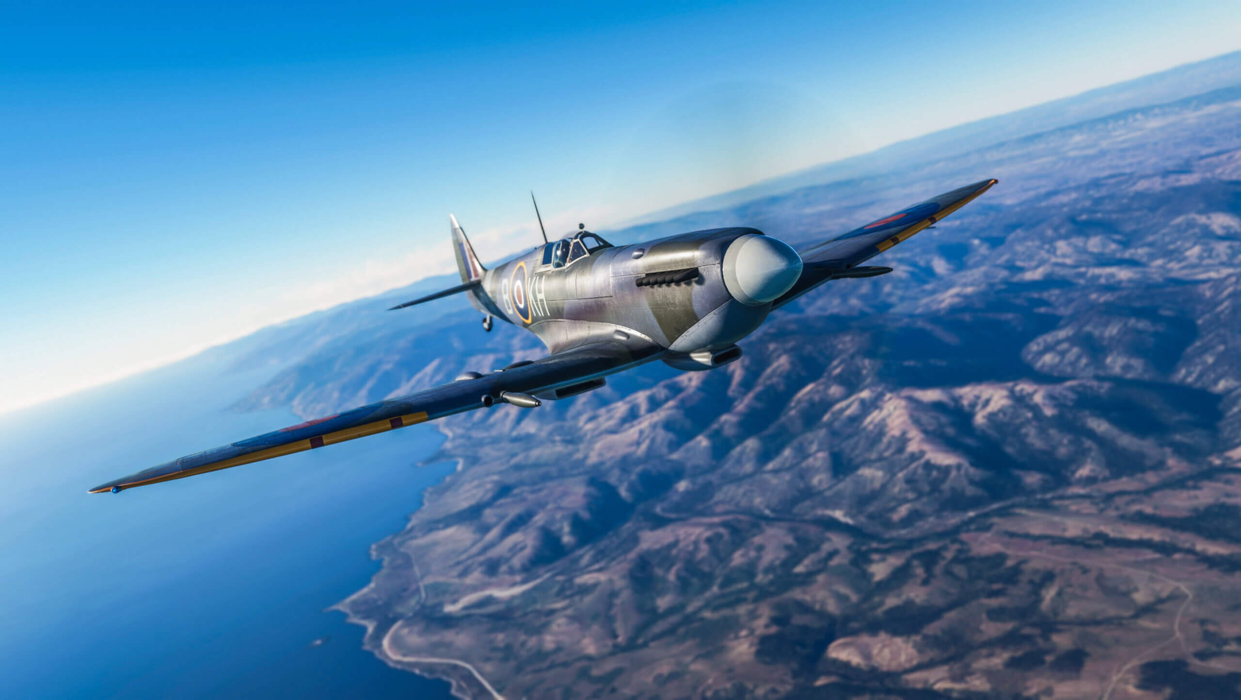 A Spitfire cruises high above a shoreline with clear blue skies above