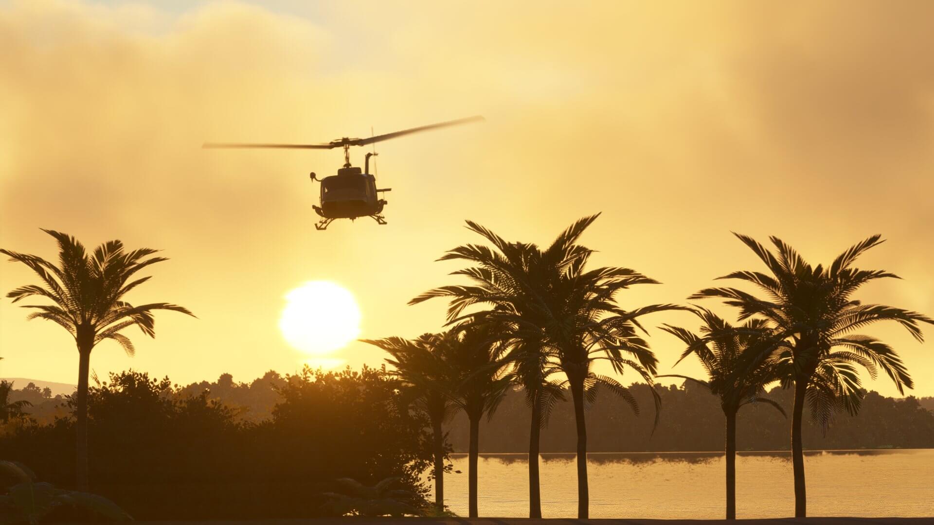 A Huey helicopter flies over some palm trees with the sun in the background