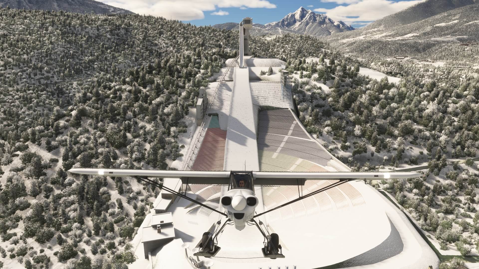 An X-Cub climbs away from a Ski Jump located in the middle of a snowy mountain range