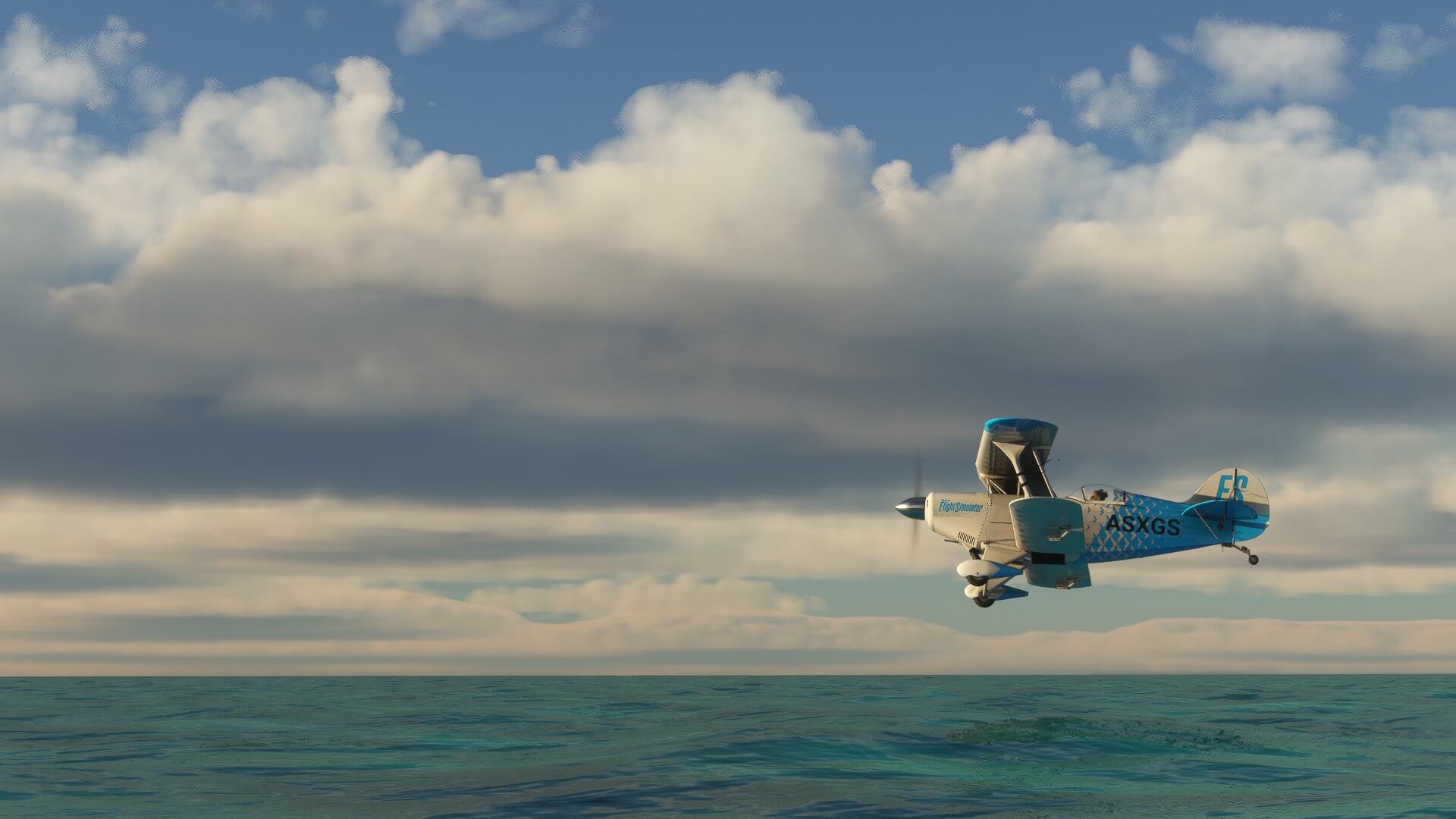 A Pitts Special flies over a blue body of water.