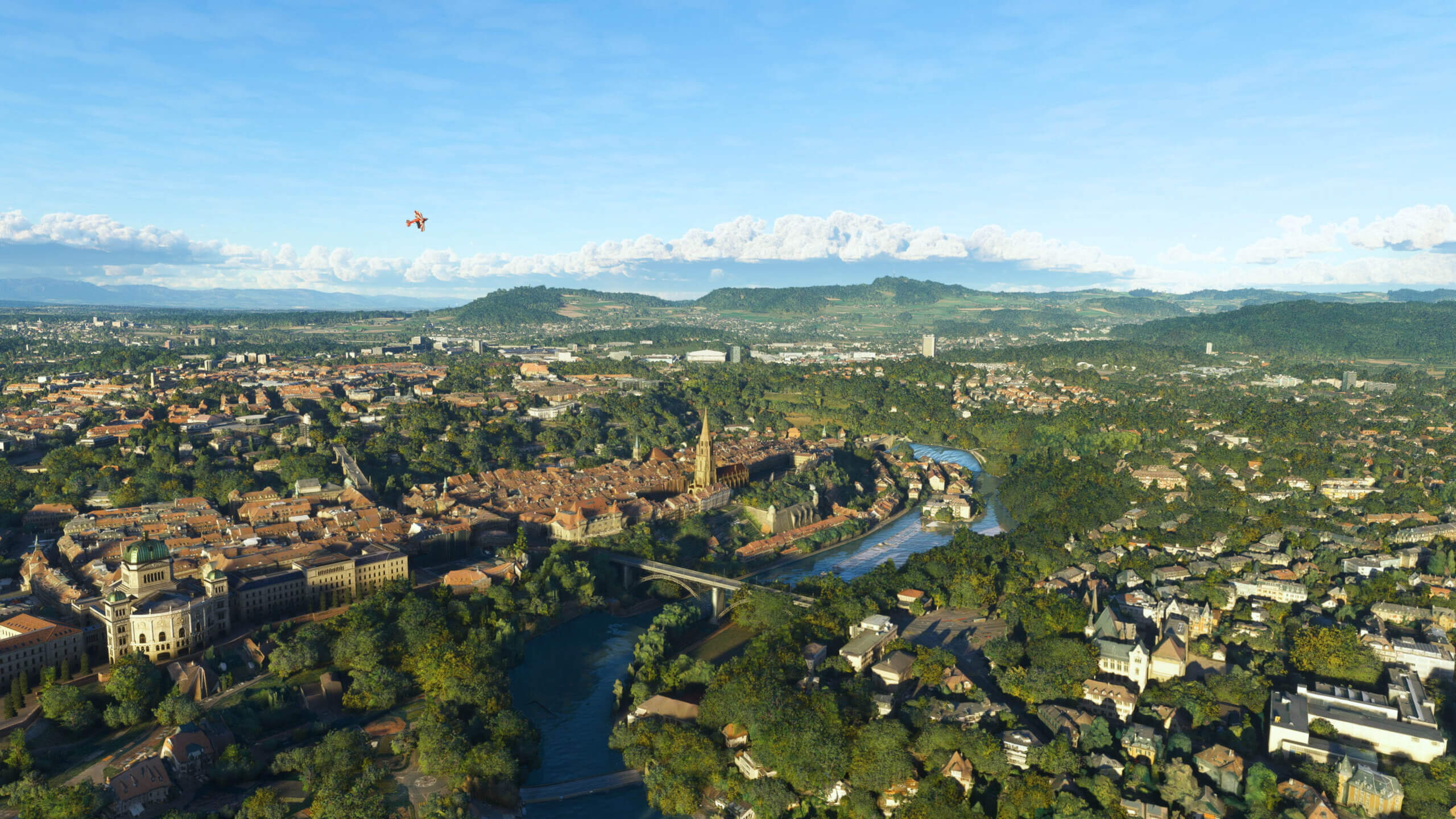 A Pitts Special flies over a European city. A church, bridge, and river are visible below.