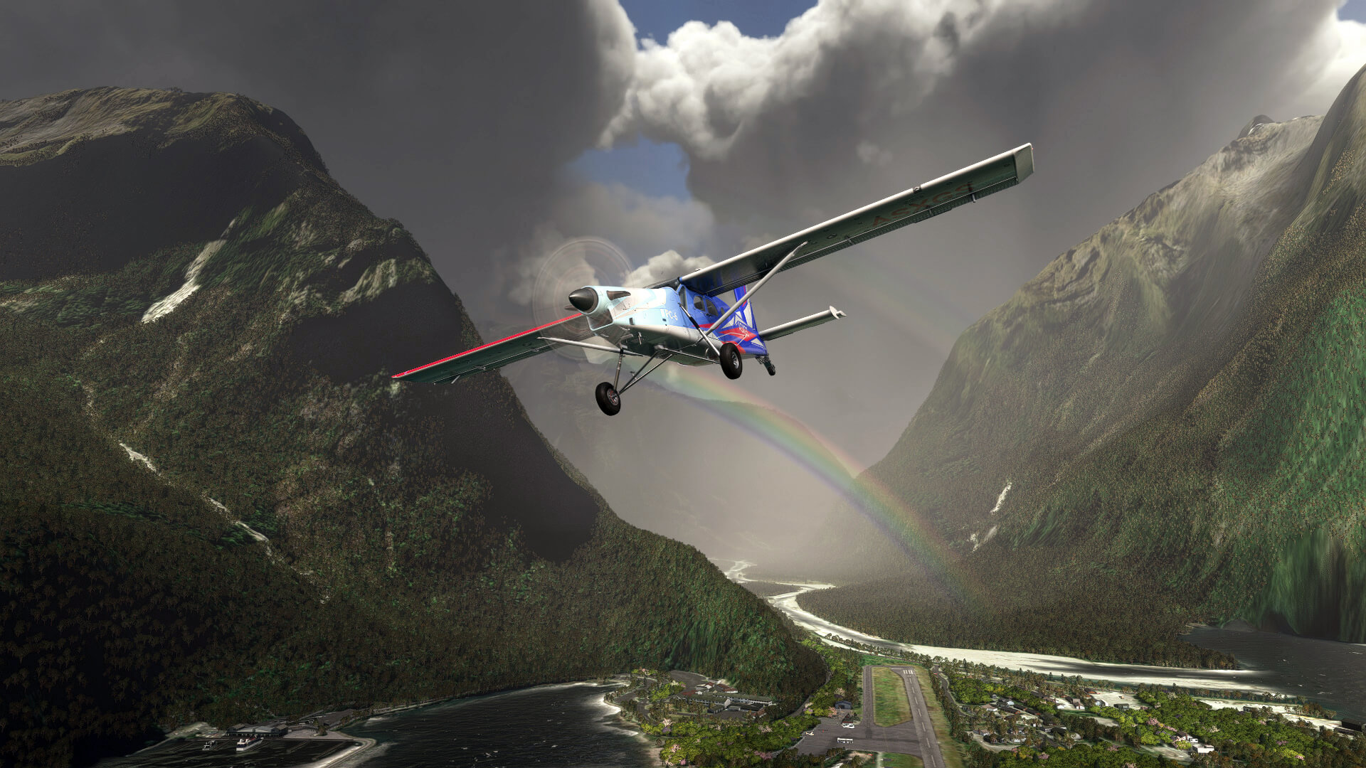 A Pilatus PC-6 crosses above an airport located in a valley, with a double rainbow in view between the terrain behind