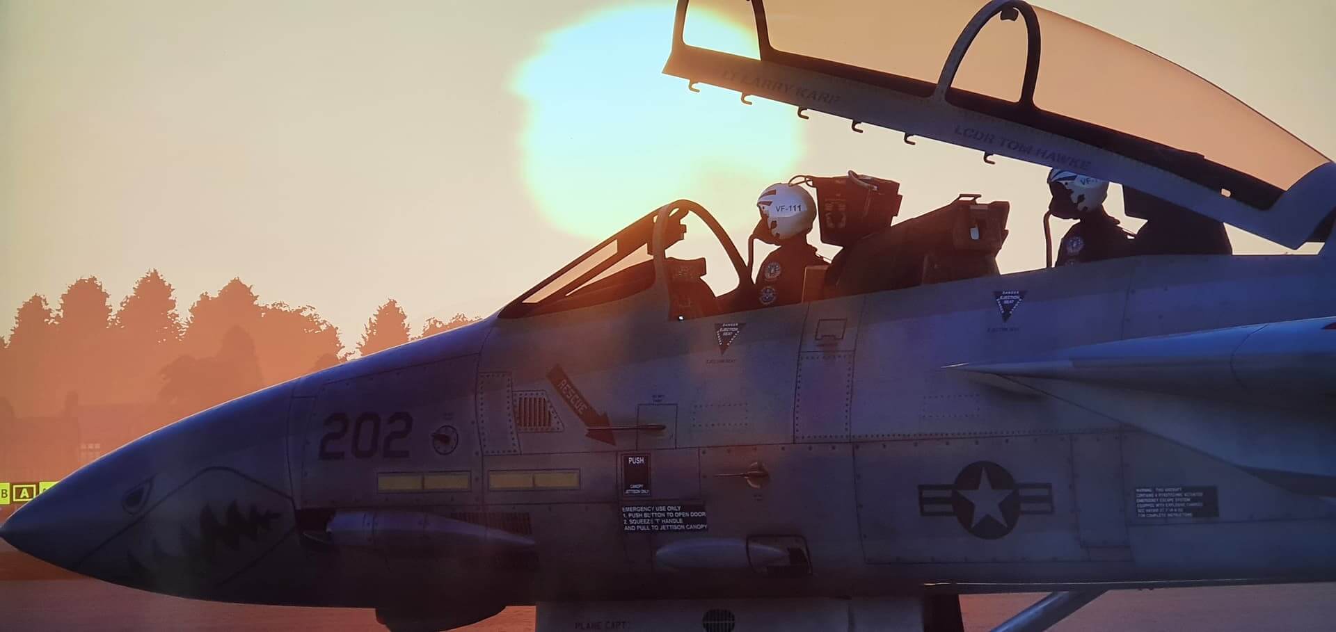 An F-14 Tomcat crew sit in the cockpit with the canopy open as the sun rises