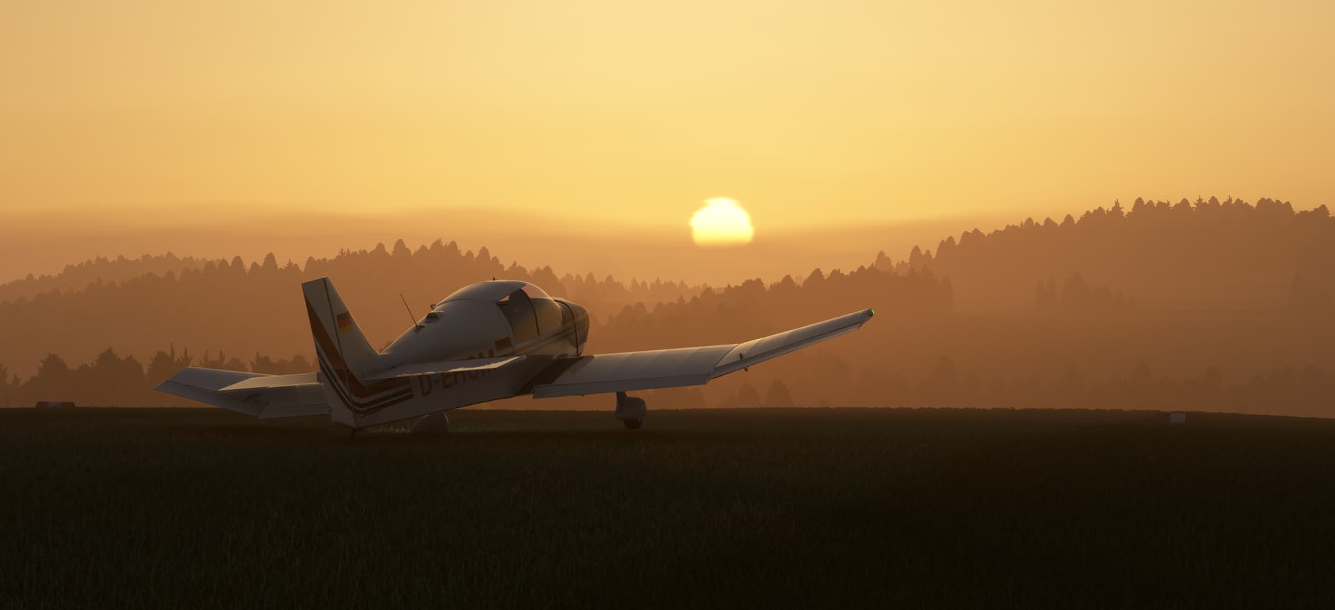 A DR-400 sits idly on a grass patch overlooking a forest, with the sun rising in the distance