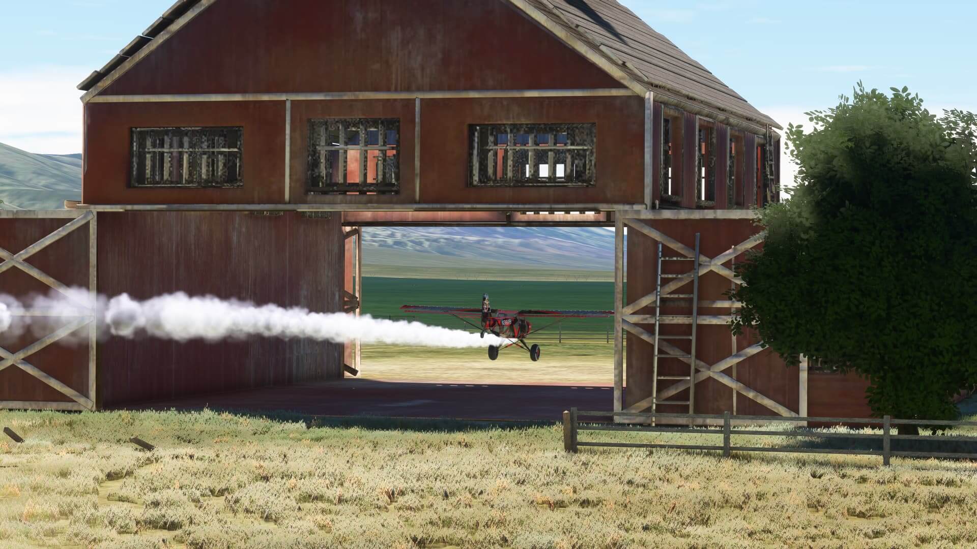 A red bush plane with smoke pluming from behind flies through a farmyard barn