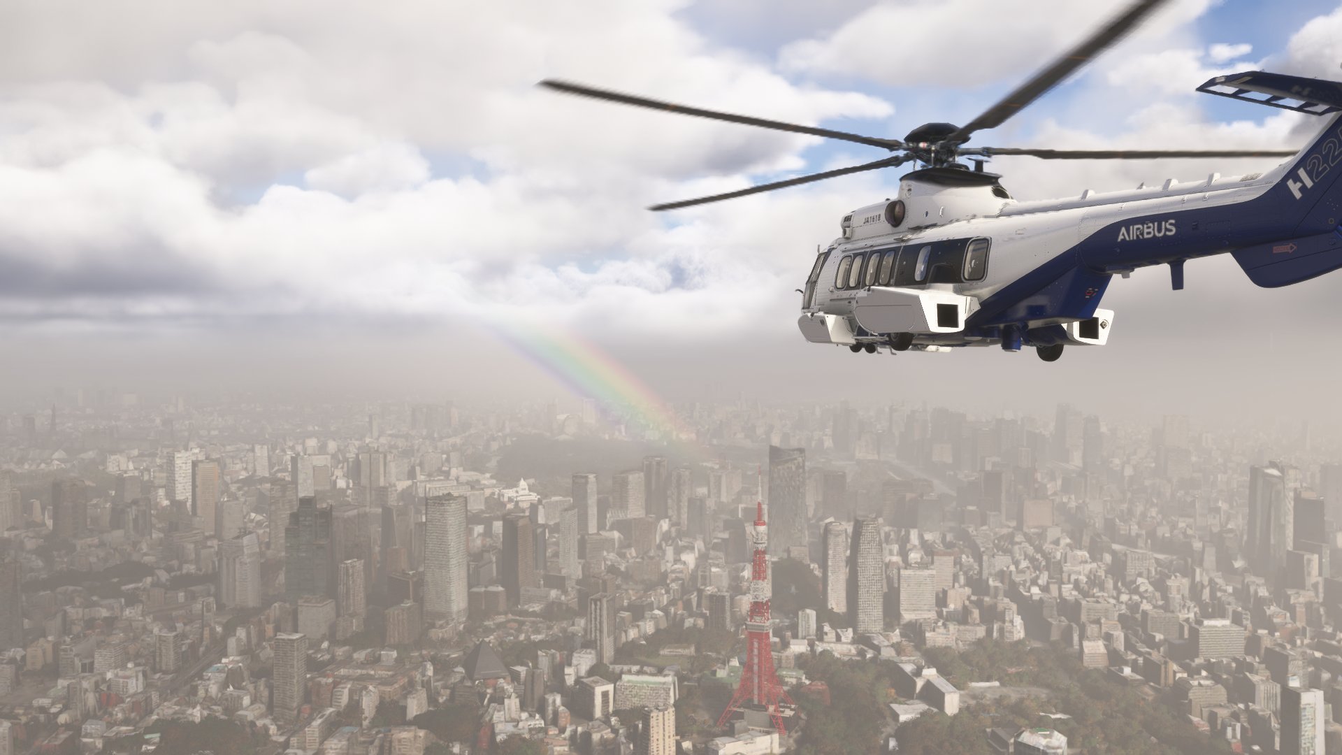 An Airbus H225 helicopter flies over a cityscape with a rainbow ahead