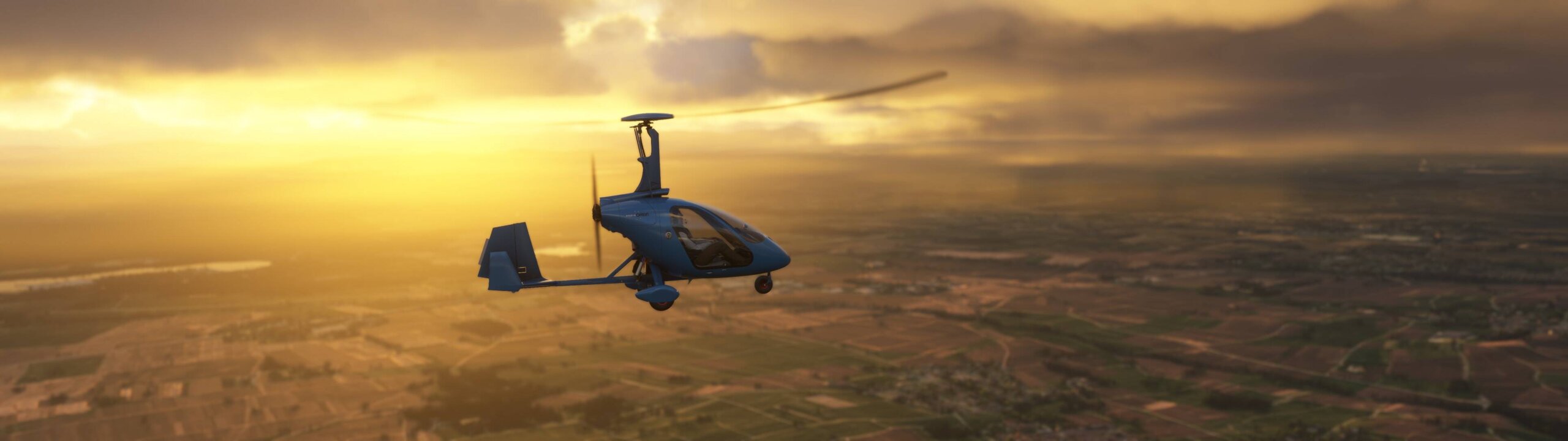 A gyrocopter in level flight with the sun setting in the distance