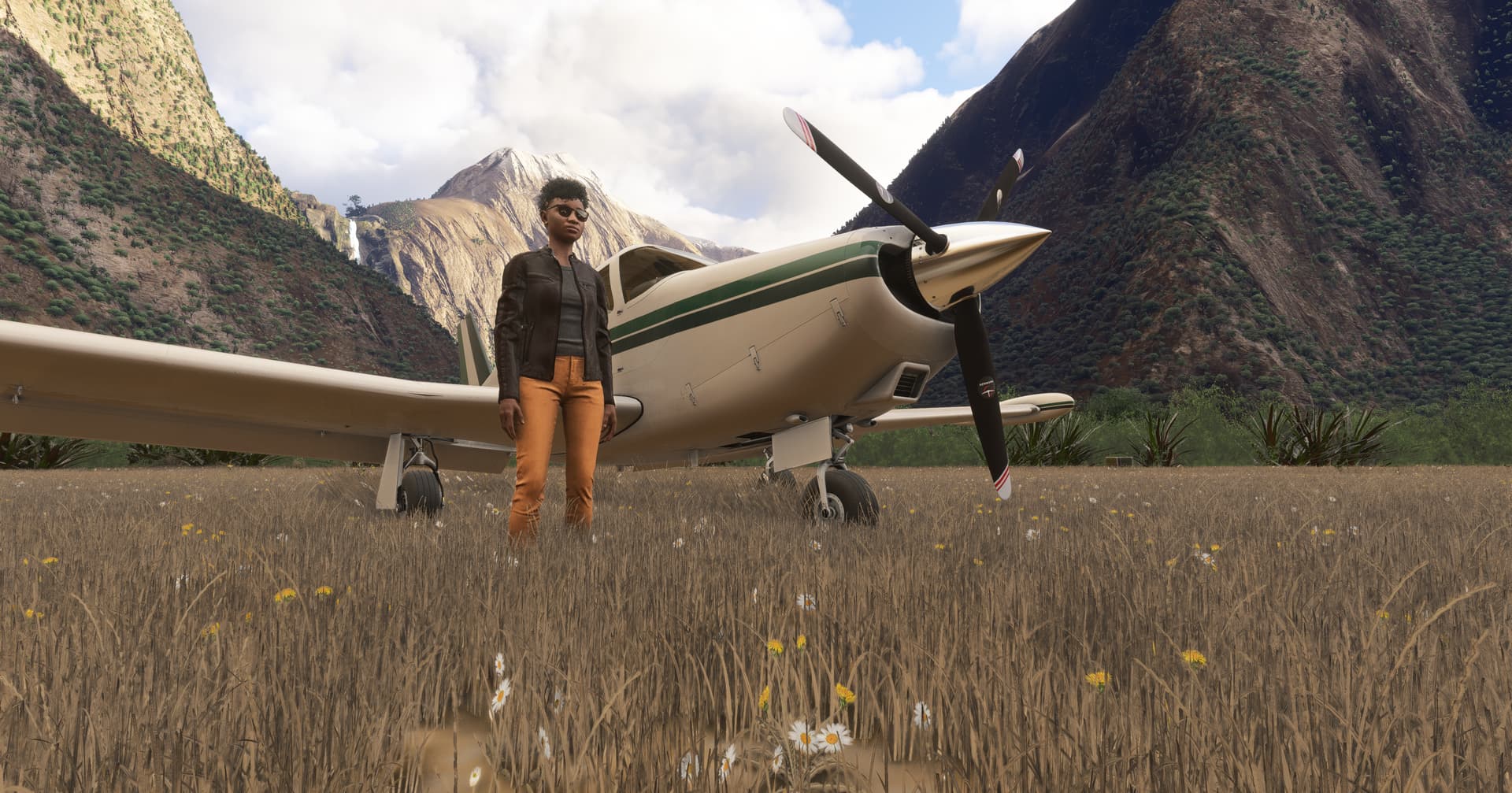 A pilot stands next to their aircraft, parked in the middle of a mountain range